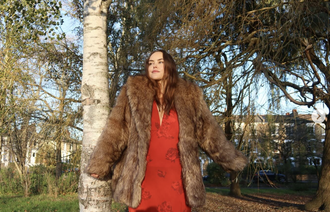 a woman wears a red dress with a faux fur coat
