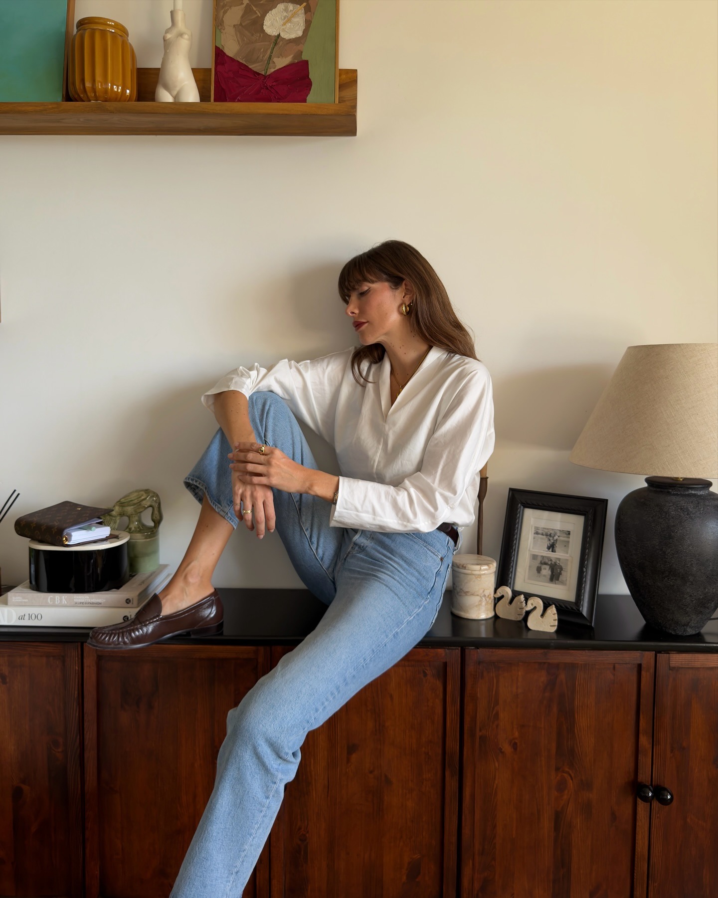 Influencer @juliesfi sits of a cabinet wearing cigarette jeans with brown leather loafers.