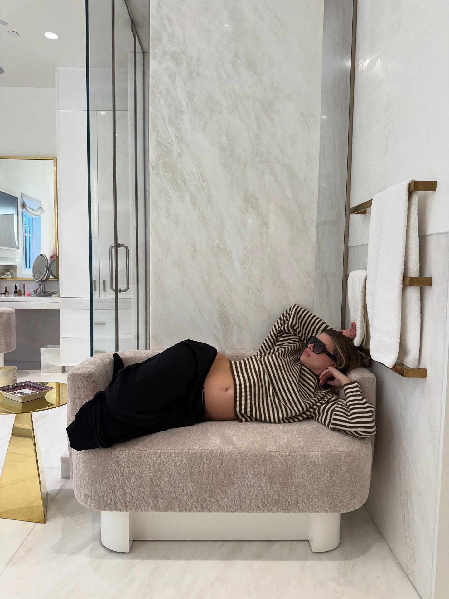 Sofia Richie Grainge lies on a sofa wearing a black and white striped knit with track pants and black sunglasses.