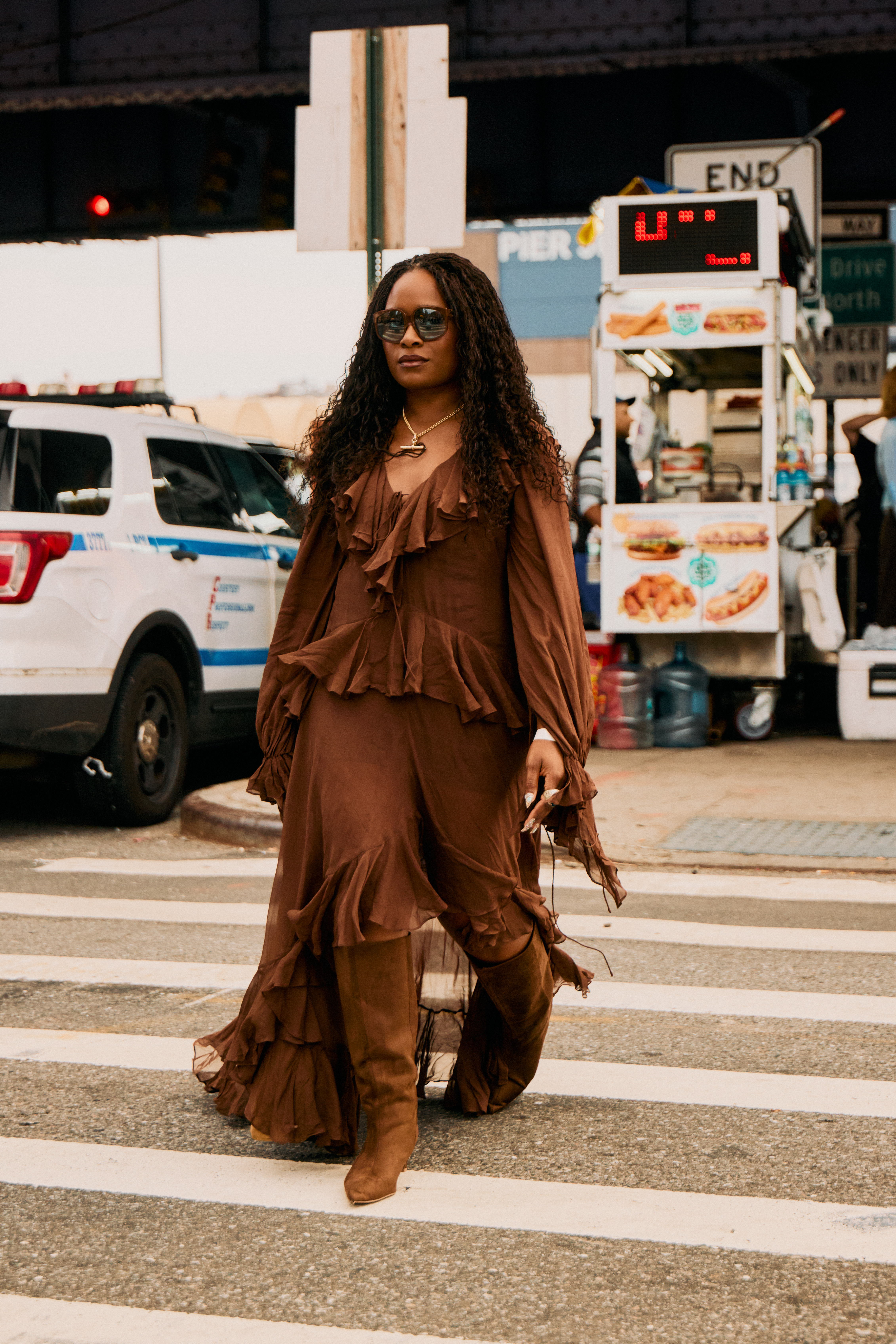 Woman in a brown boho-chic ruffle dress, brown suede boots, and oversized sunglasses.