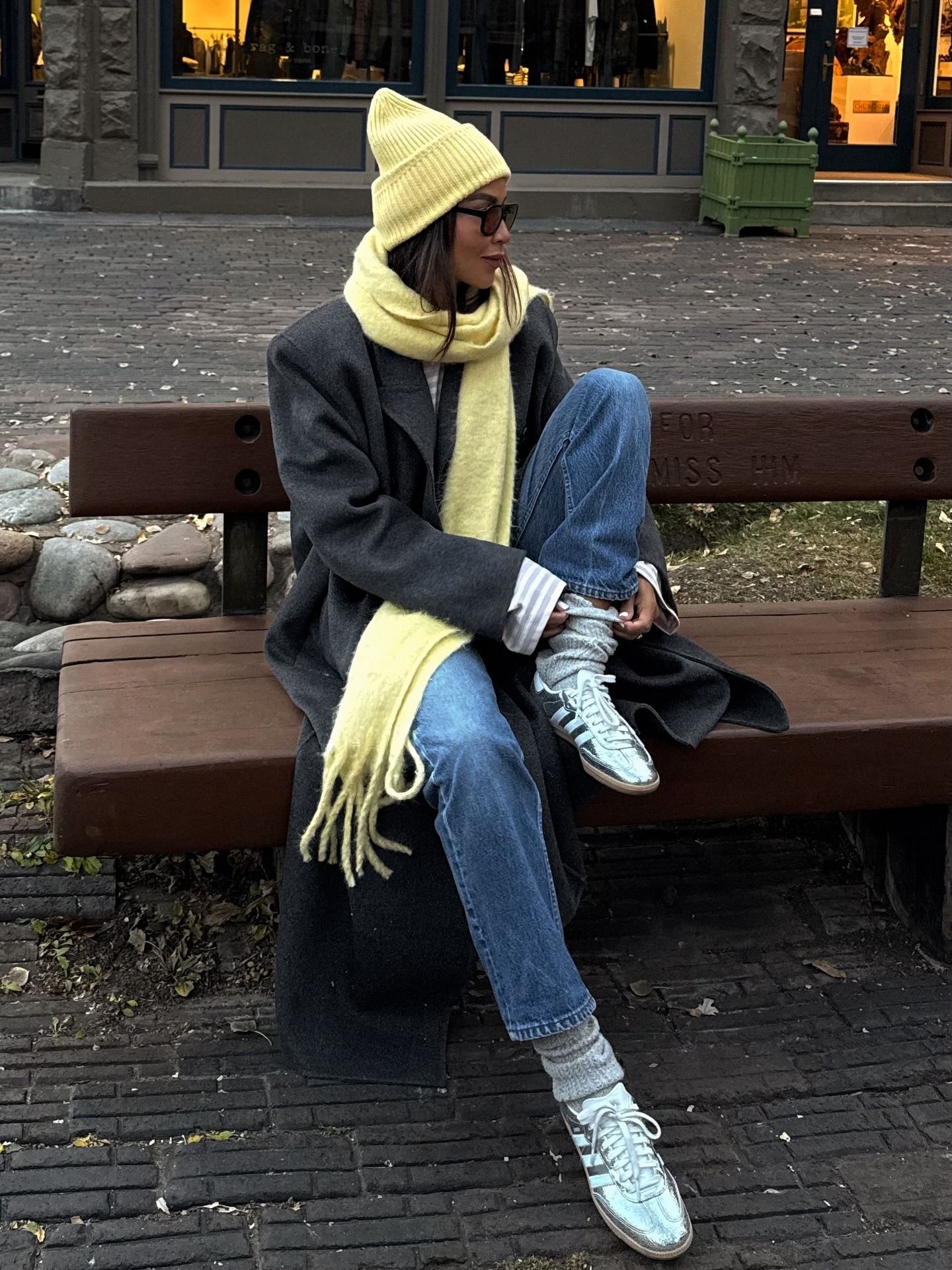 Fashion person Julie Sari&amp;ntilde;ana @sincerelyjules wears a leather trainer outfit. She wears a metallic trainer, jeans long coat and butter yellow hat and scarf.