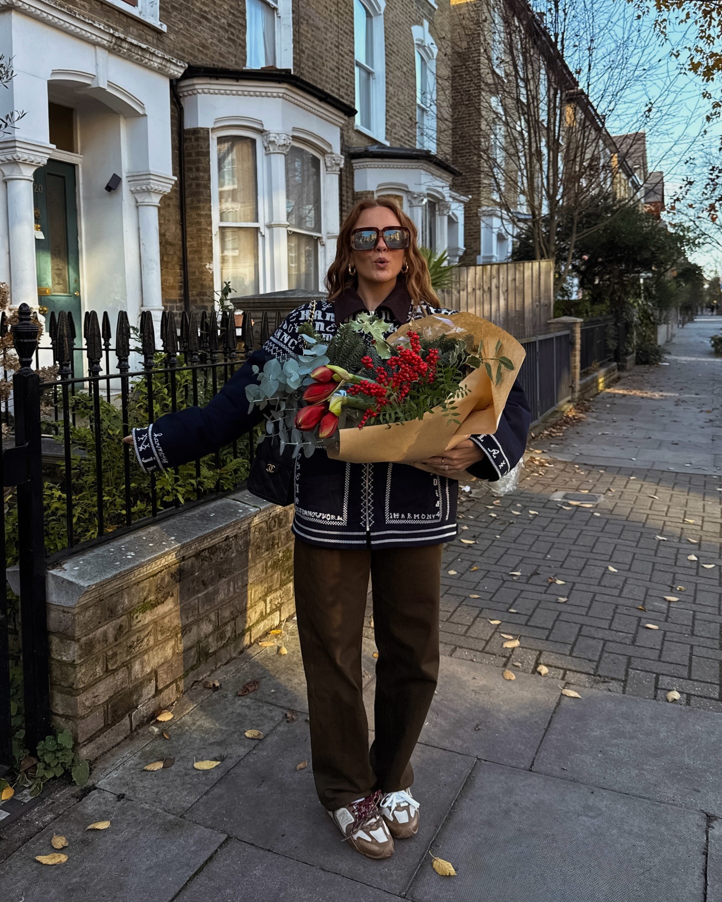 Fashion person Rebecca Ferraz-Wyatt @rebeccaferrazwyatt wears a leather trainer outfit. She wears a printed jacket with suede trainers, brown trousers and a Chanel 25.