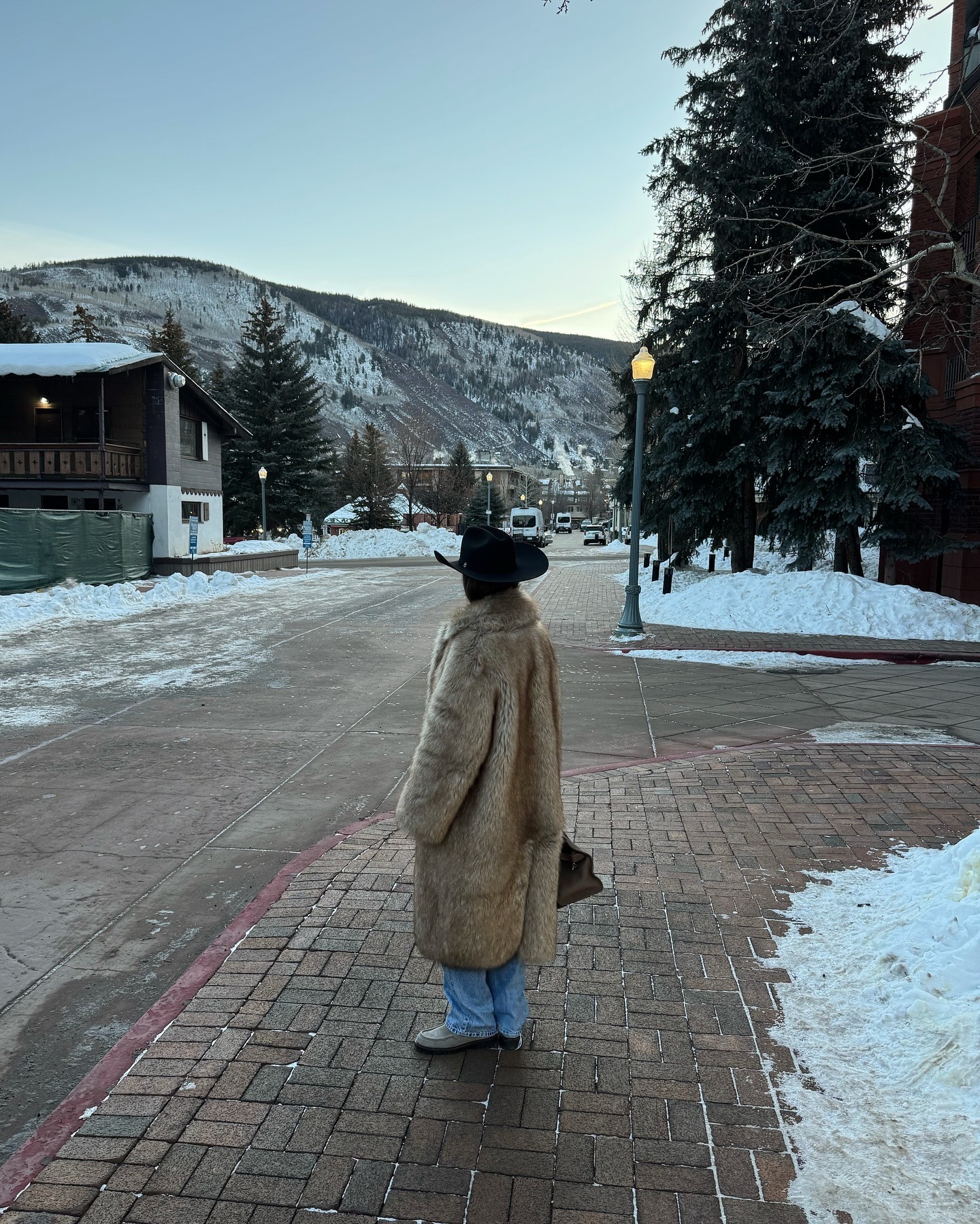 A woman wears a cowboy hat, fur coat, jeans, and suede loafers.
