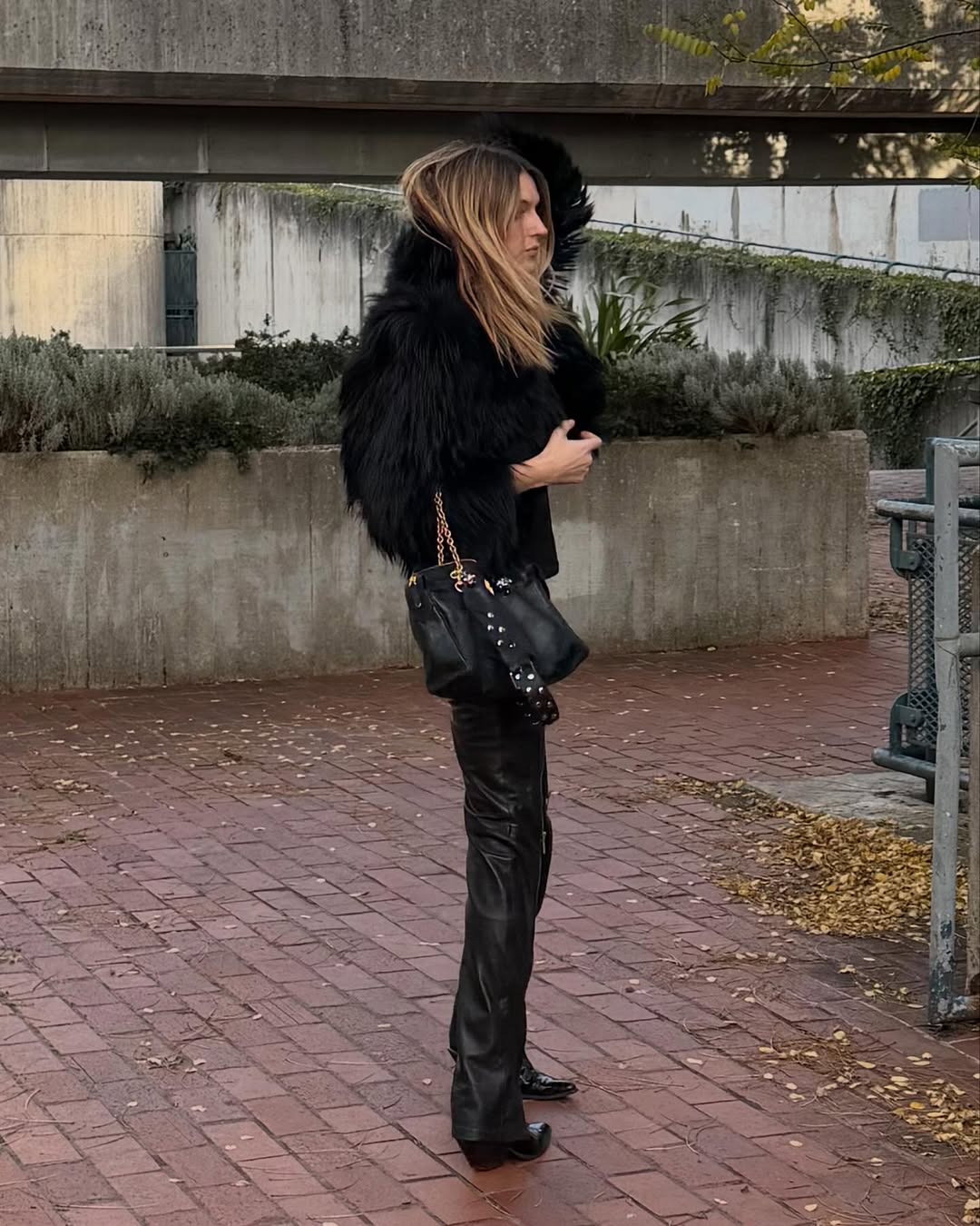 A woman wearing black pants with a black faux fur jacket and boots.