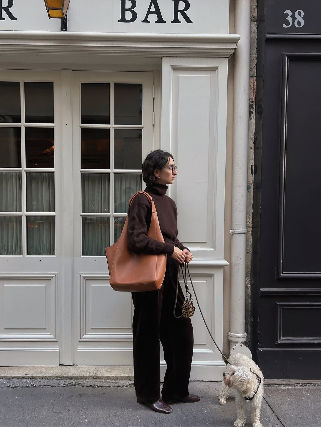 A woman wearing black pants with a brown sweater and leather boots while walking a dog..
