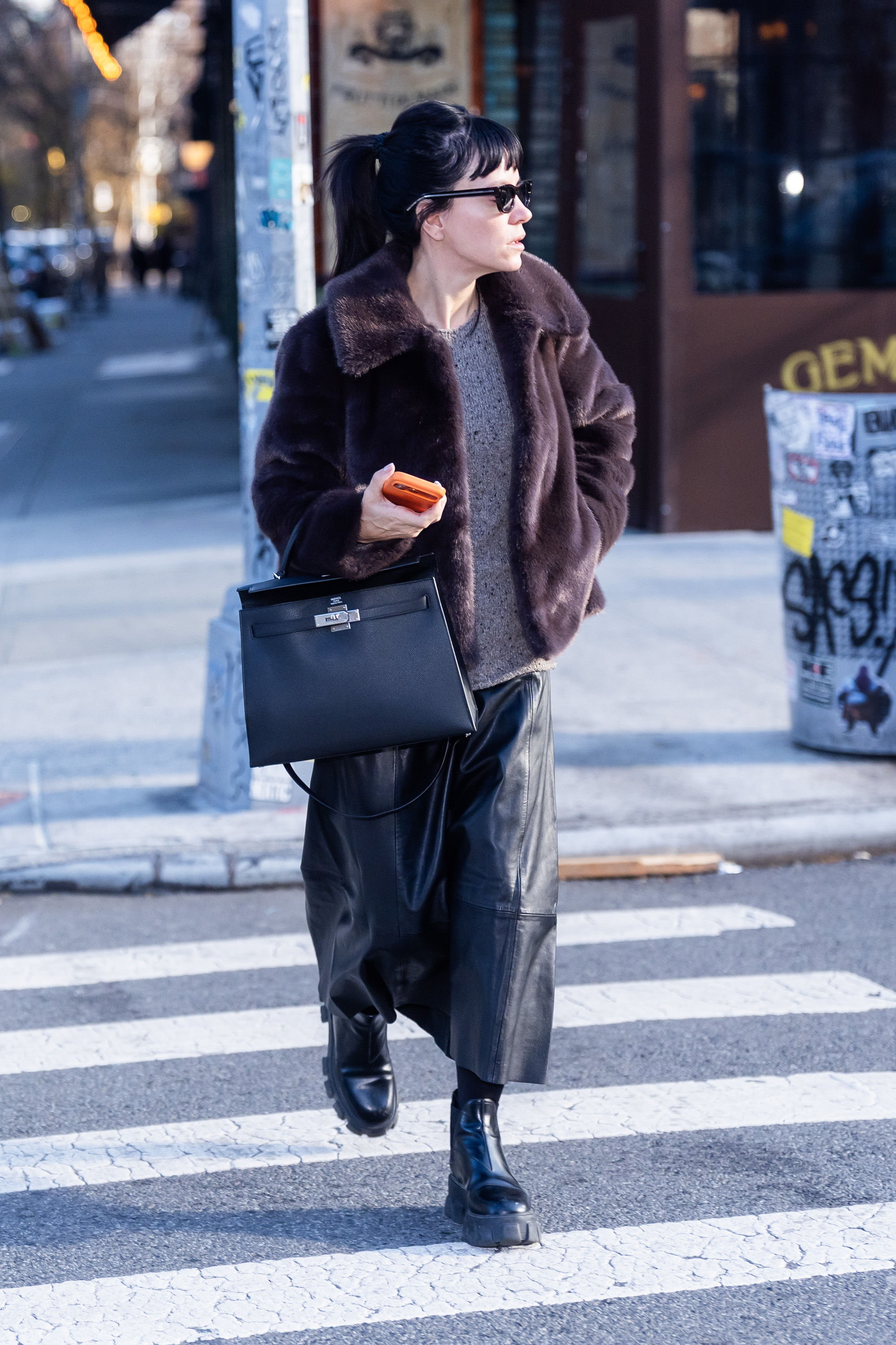 Lily Allen wears Hush fur jacket with a grey jumper a black leather skirt black lug-sole boots and a black Hermes bag and black sunglasses.