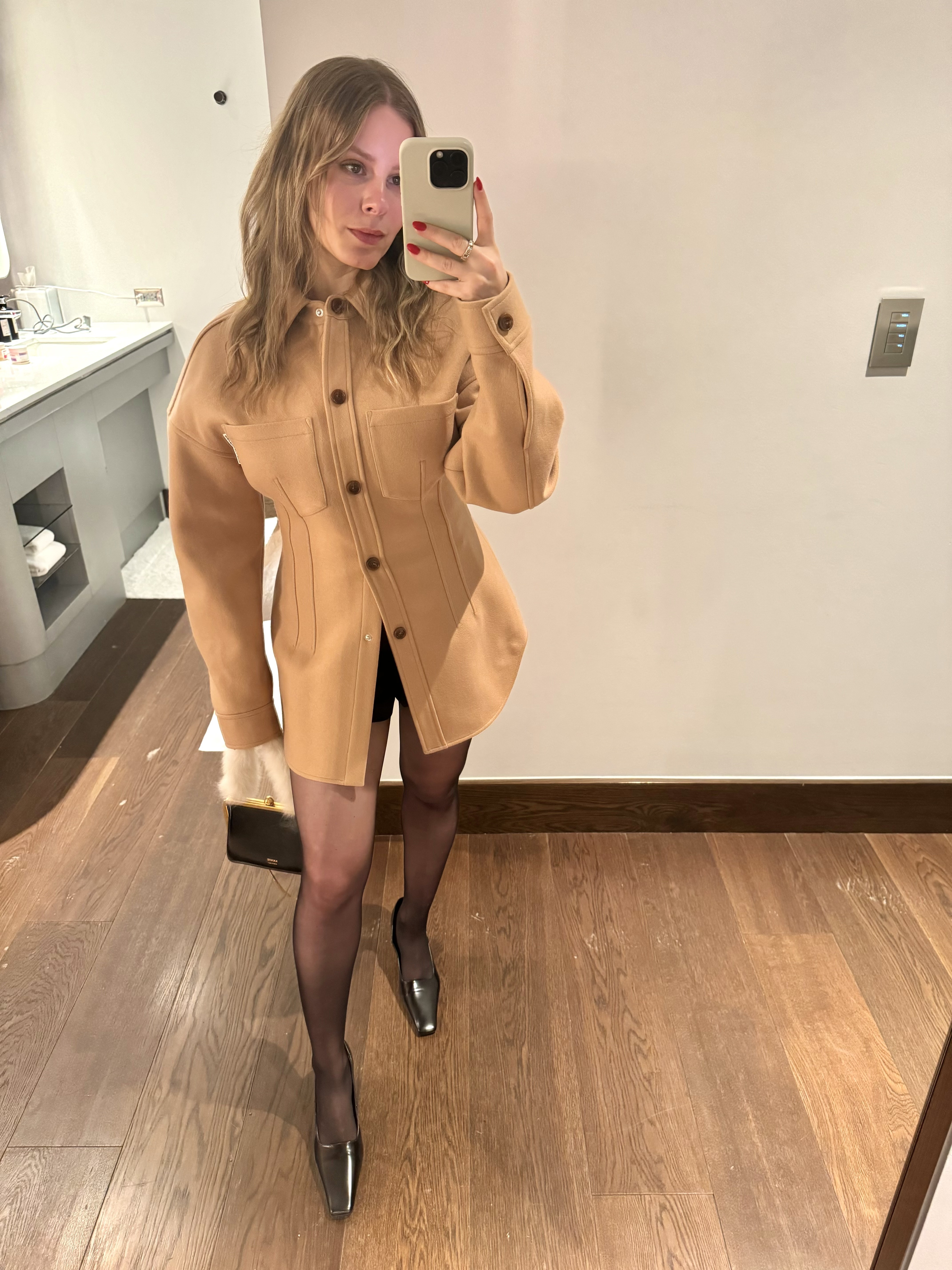 Nikki wears a beige button-up jacket, sheer tights from wolford, and black heels.