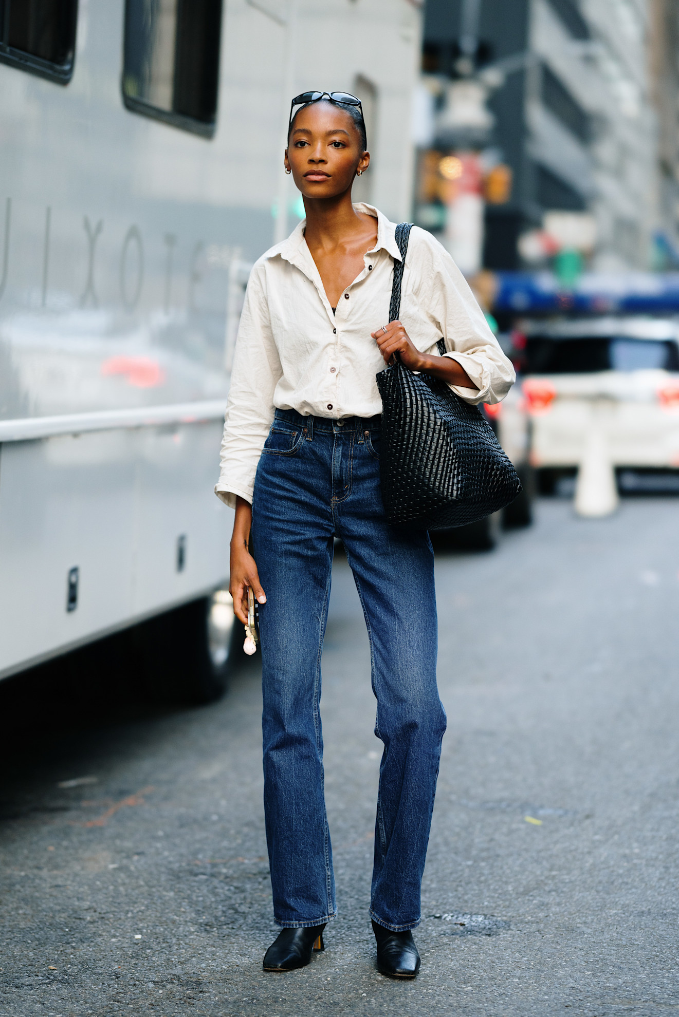Person in a white button-down and jeans with a large black tote and heeled boots.