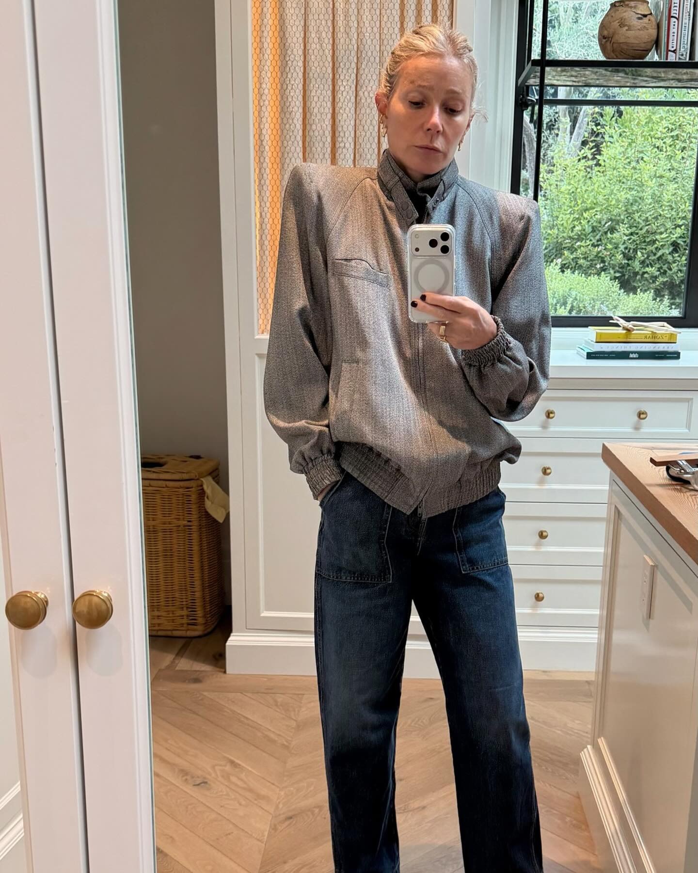 Gwyneth Paltrow takes a mirror selfie wearing a high-neck jacket with dark wash jeans.