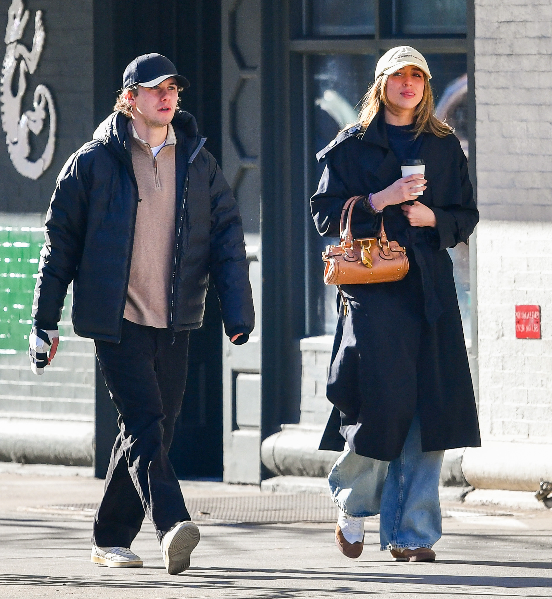 Tate McRae wears a black trench coat, baseball cap, chloe paddington bag, wide-leg jeans, and chloe sneakers.