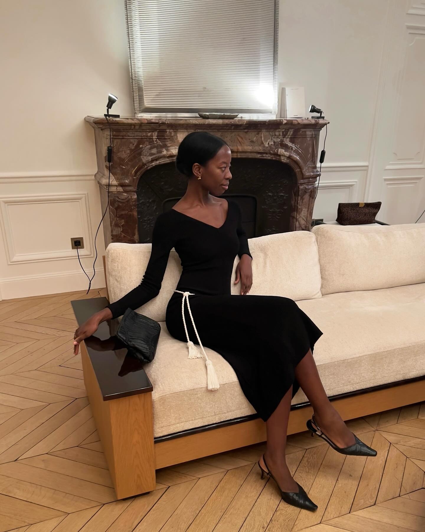 A woman in a black dress and slingback shoes lounging on a couch.