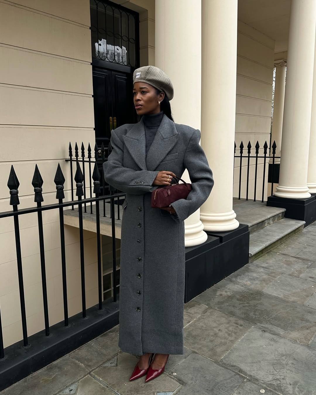 A woman in a tailored gray coat with burgundy accessories and a Miu Miu hat.