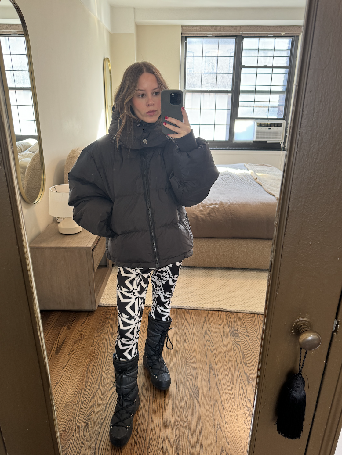 Nikki wears a black puffer jacket, leggings, and snow boots.