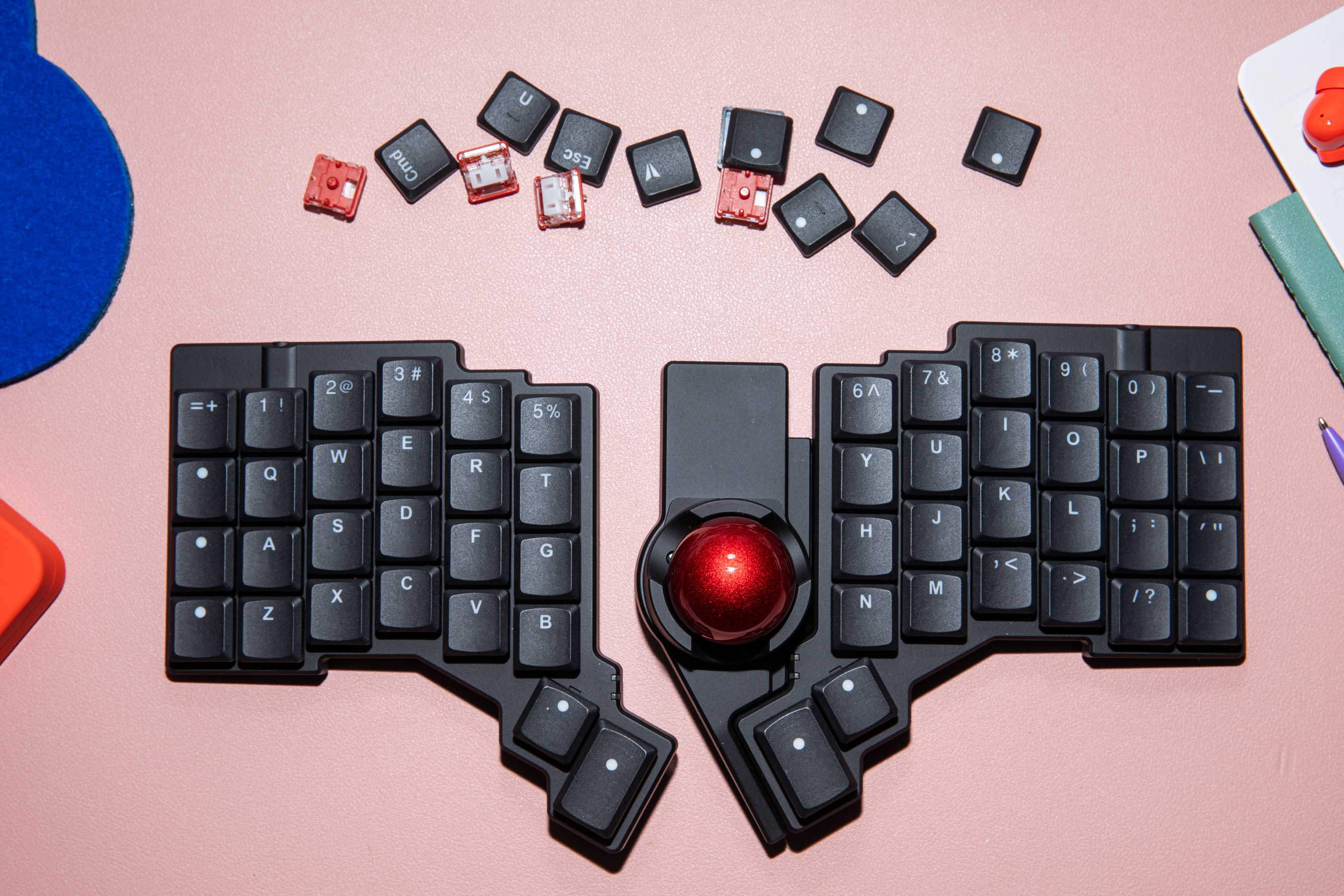 ZSA’s Voyager keyboard and Navigator trackball on a pink background.