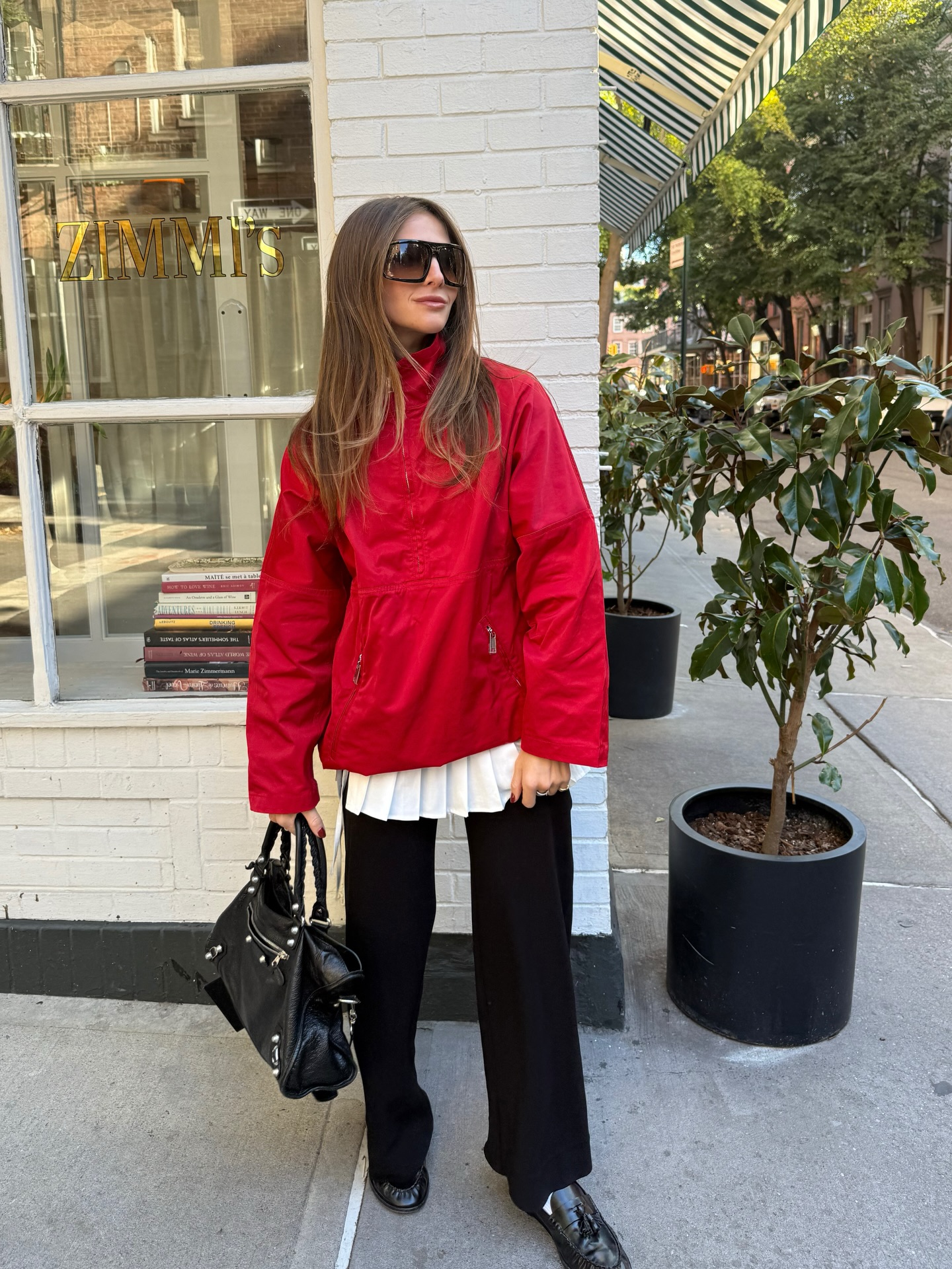 Hannah wears oversize sunglasses, a red jacket, and black pants.