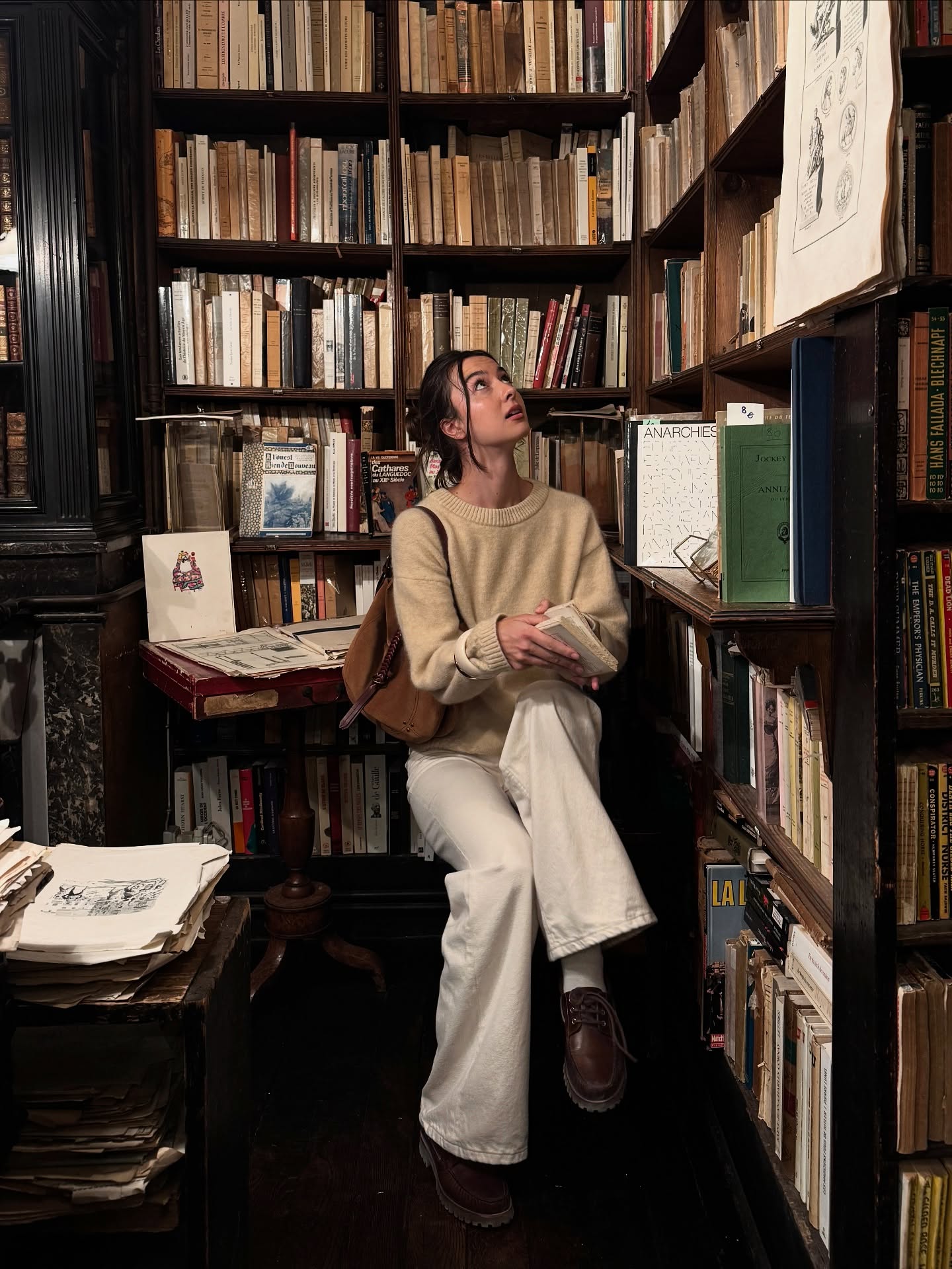 Lara wears a fun, messy updo with a beige sweater and white jeans.