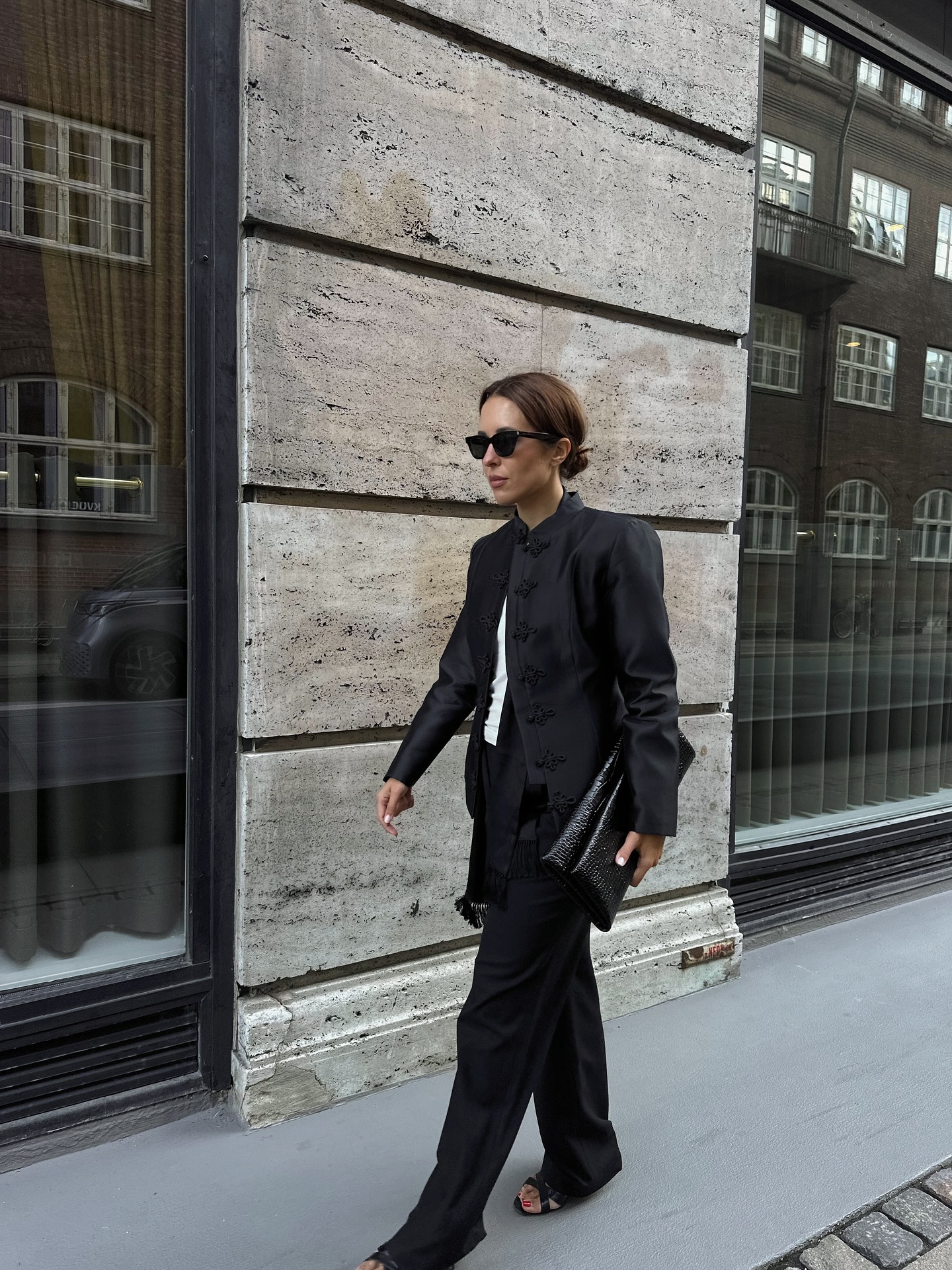 Influencer @deborabrosa wears a high-neck blazer with black straight-leg trousers and black strappy heels.