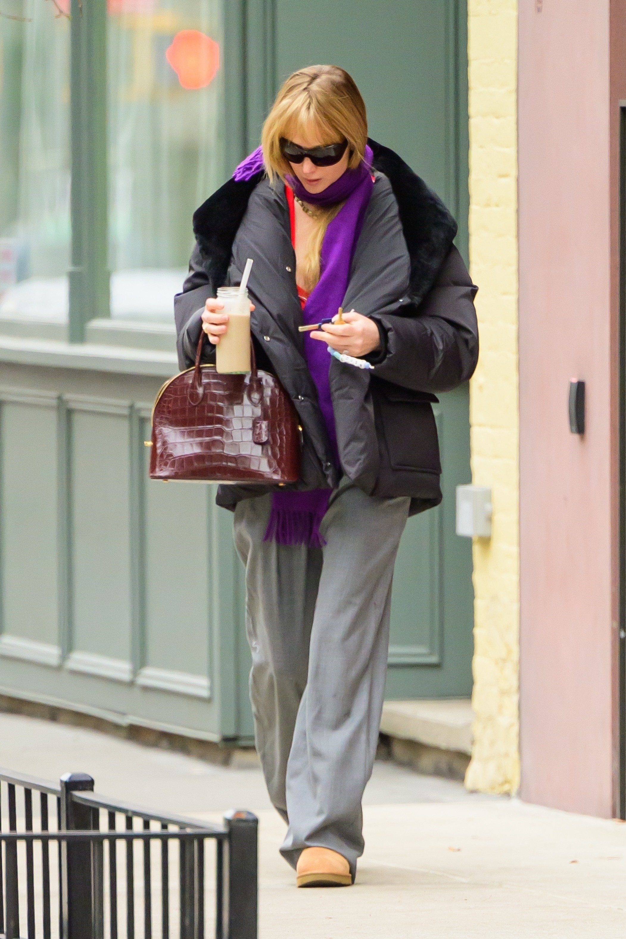 Jennifer Lawrence wears a black puffer jacket, purple scarf, brown croc bag, gray trousers, and Chestnut Uggs.