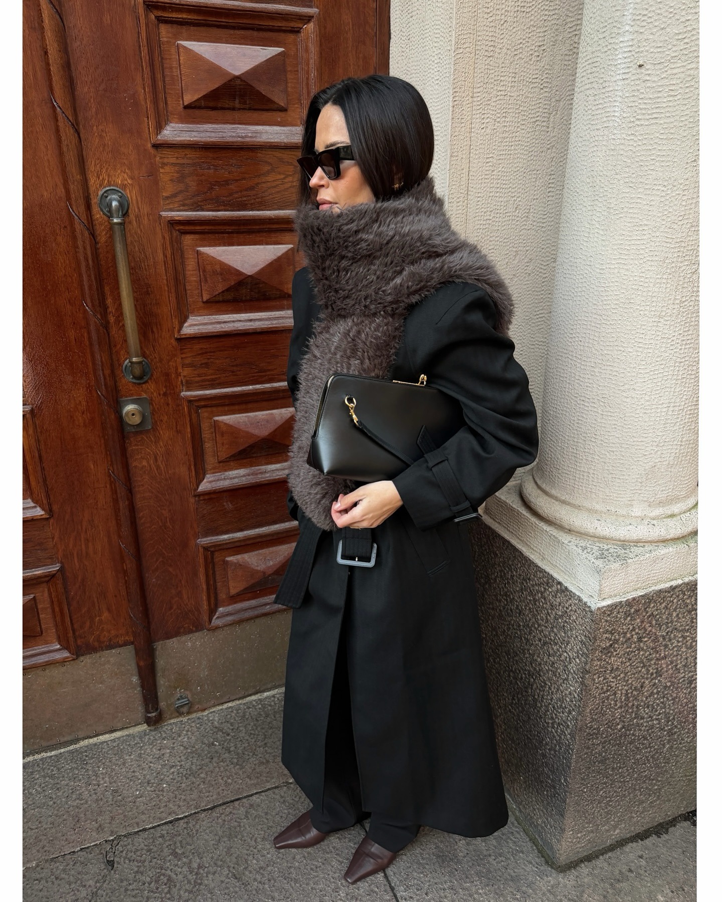 @johannapiispa wears a long belted coat with a fur scarf, black bag, and brown pointed-toe boots.
