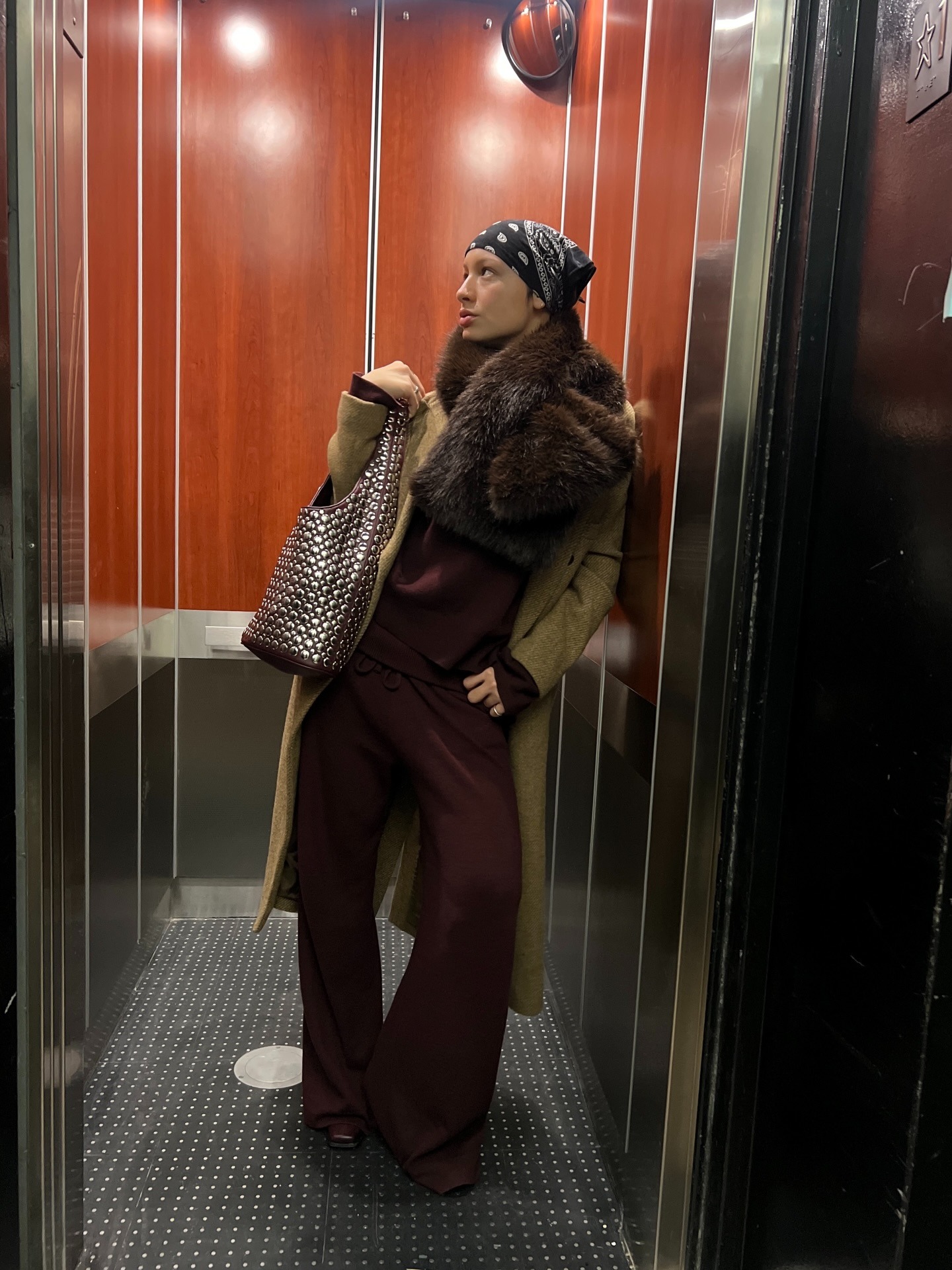 @aishafarida wears a burgundy ensemble with an colored coat, fur scarf, bandana, and studded tote.