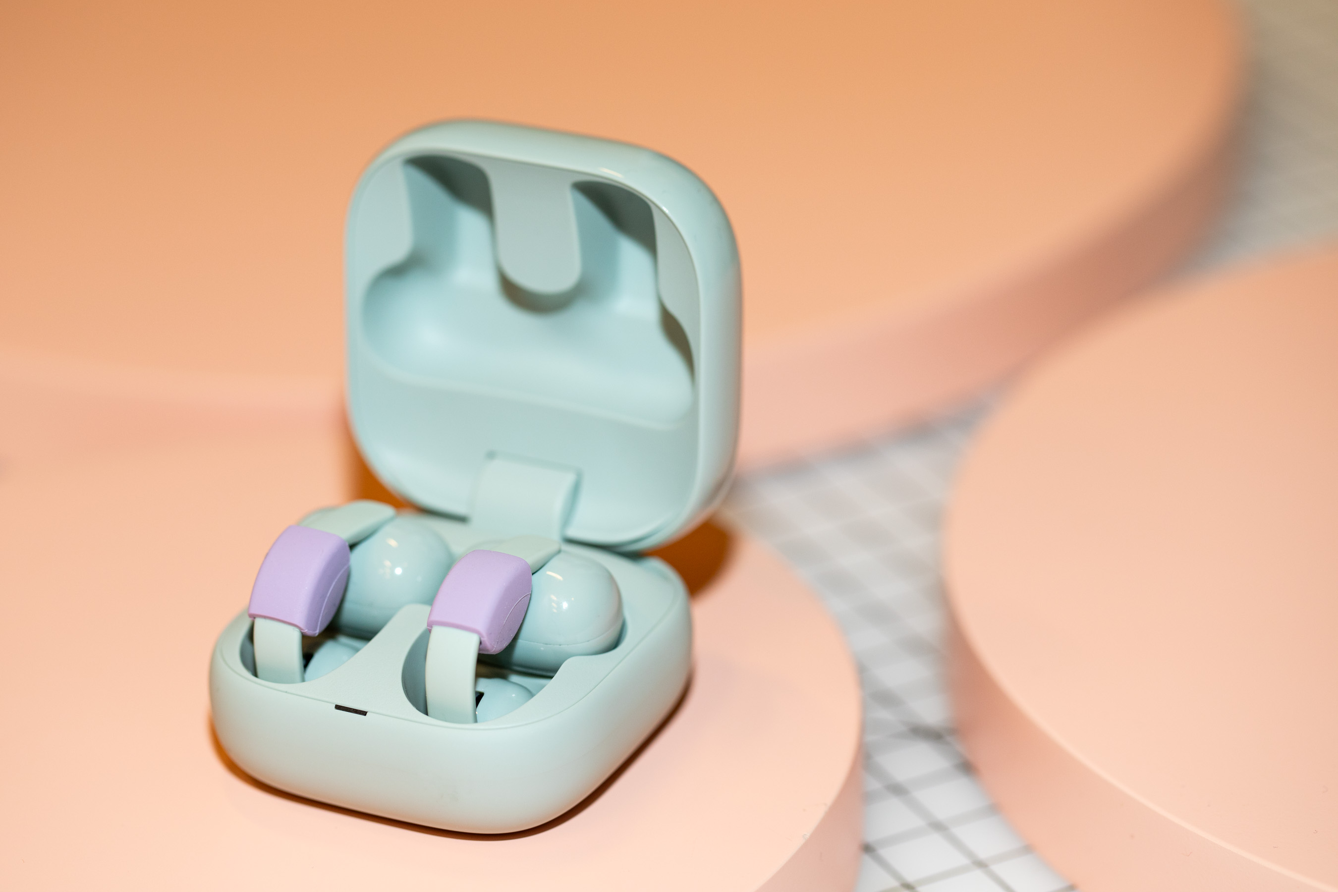 Sony LinkBuds Clip in their open case on a peach surface.