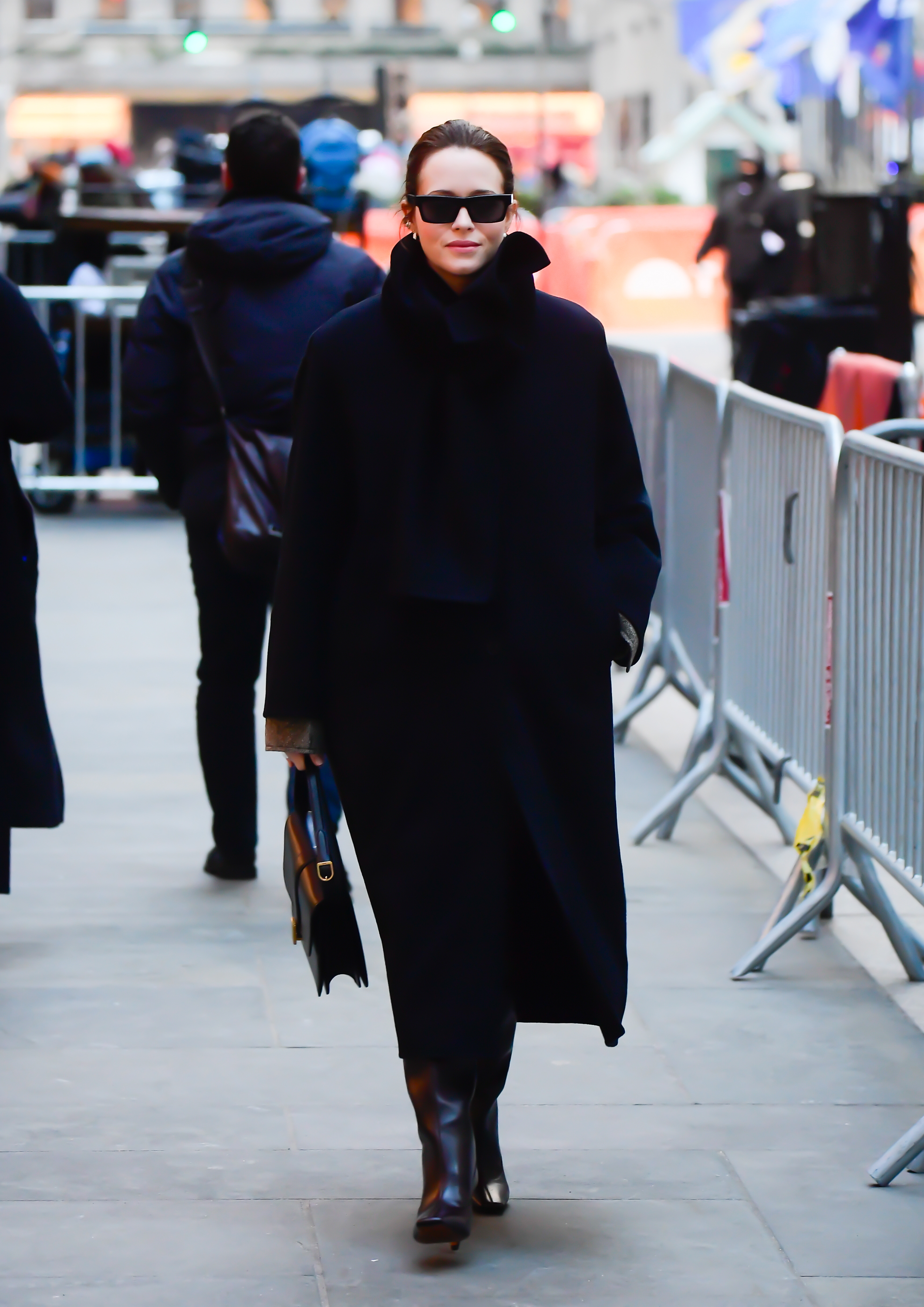 Claire Foy walks down the street wearing a black coat with brown heels boots and a black leather bag.