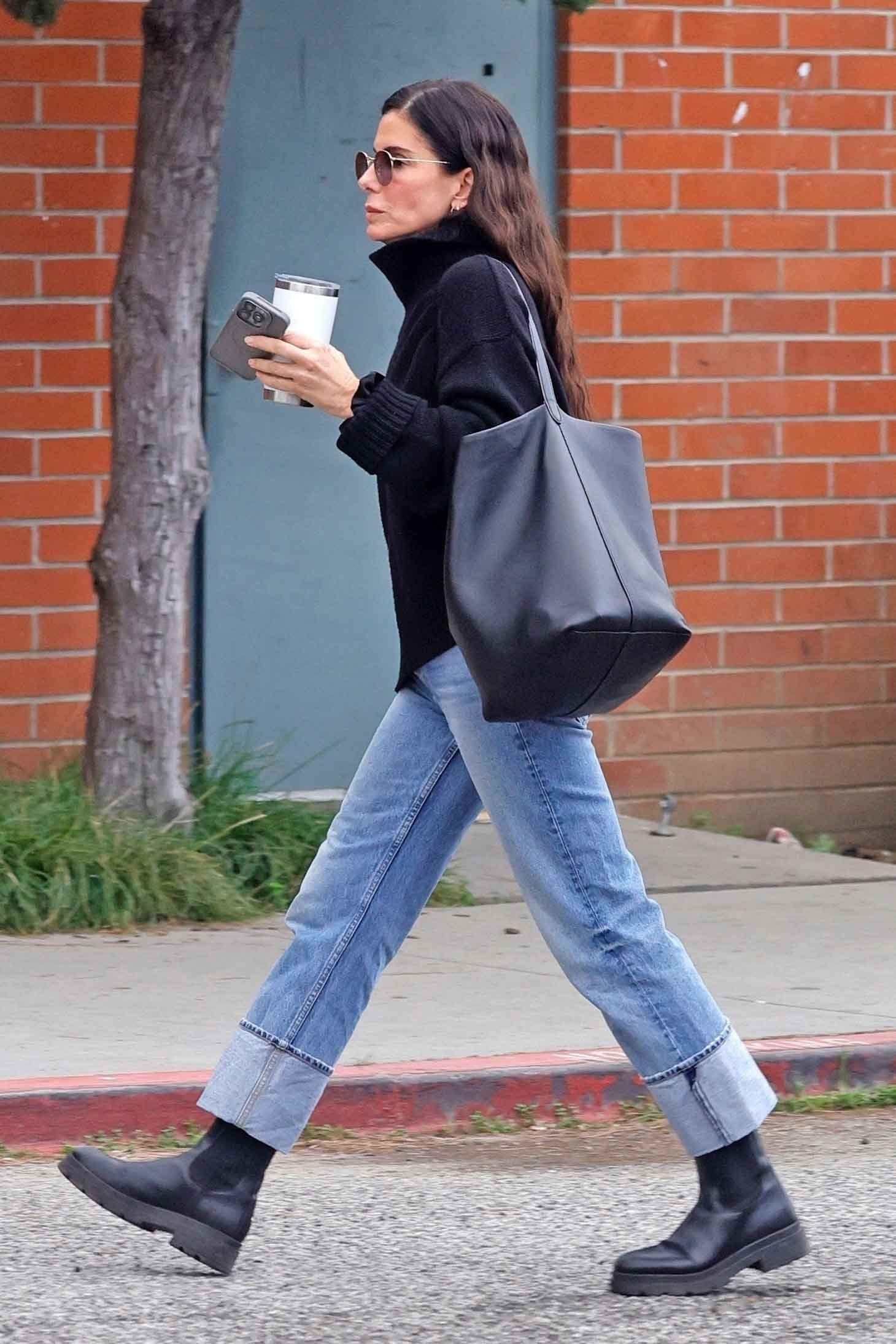 Sandra Bullock steps out in her signature understated style, wearing black knit turtleneck sweater paired with cuffed straight-leg jeans and sleek black Chelsea boots.