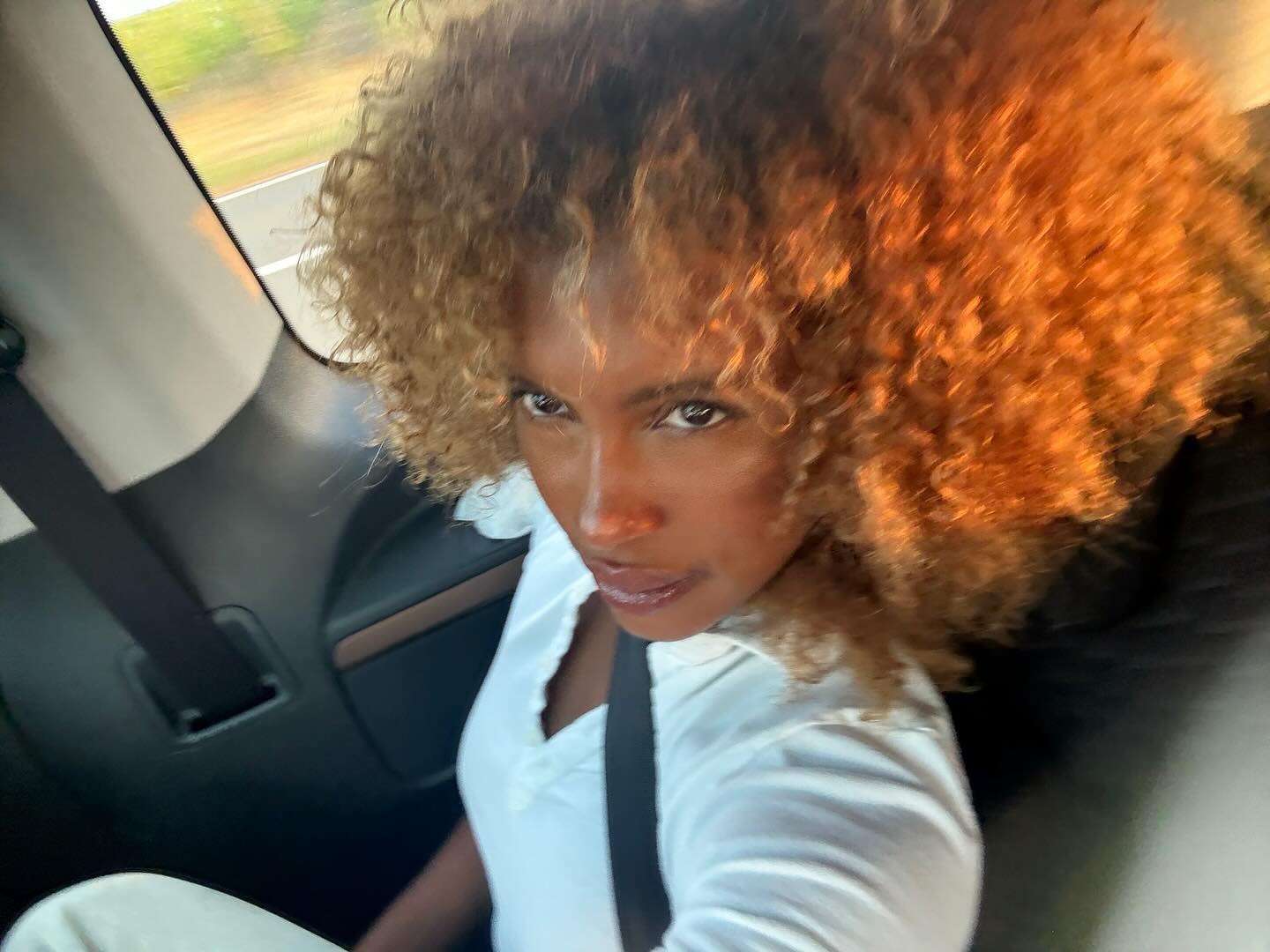 A woman with curly hair and a wispy fringe taking a selfie in the car