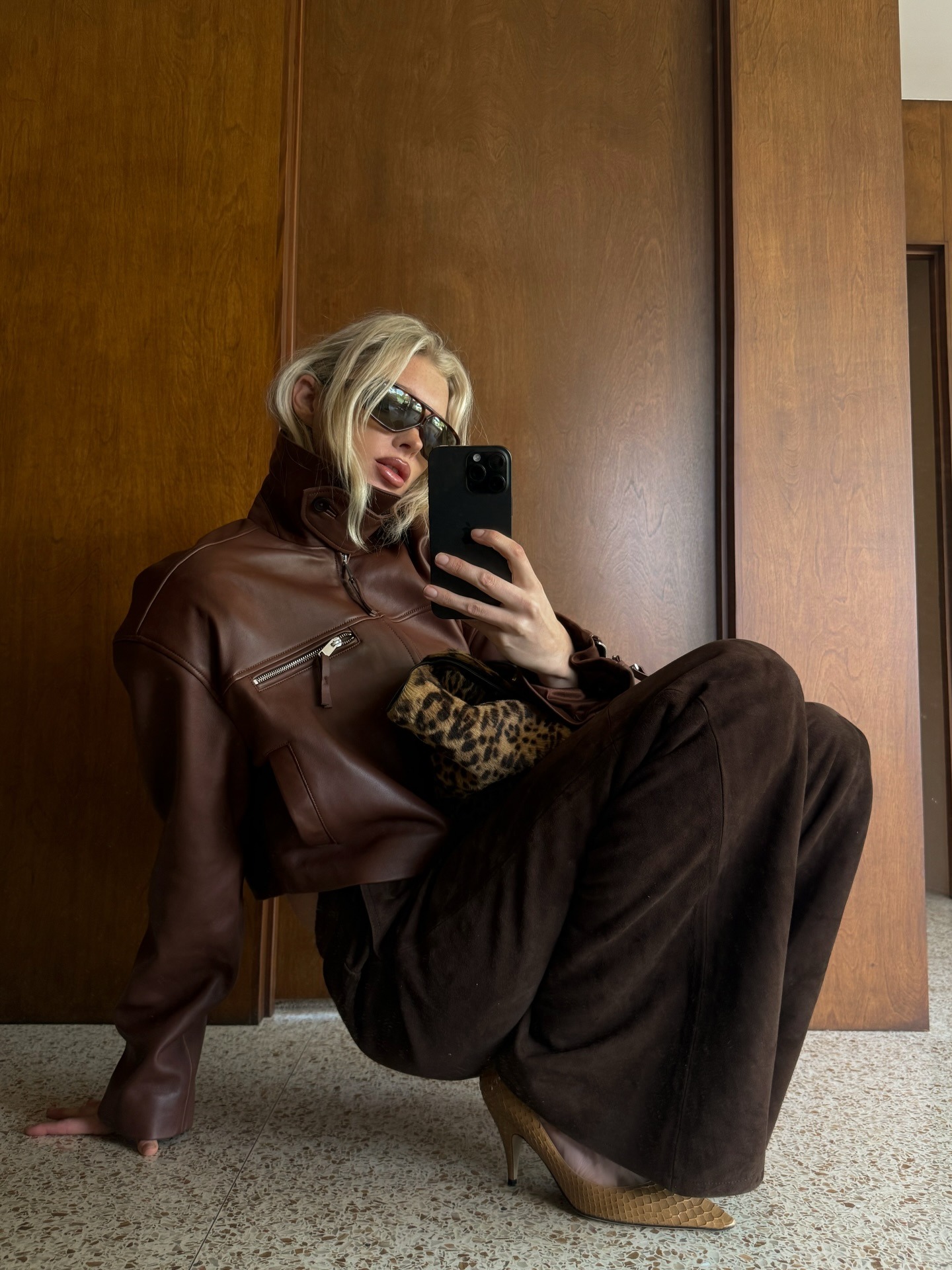 Elsa wears a brown leather jacket with brown suede pants, kitten heels and a leopard bag.