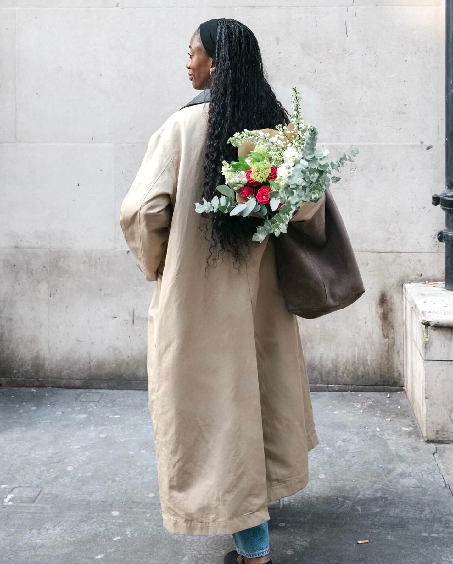 British style influencer Liv Madeline wearing a barn coat, a brown suede tote filled with flowers, jeans, and Mary Jane flats
