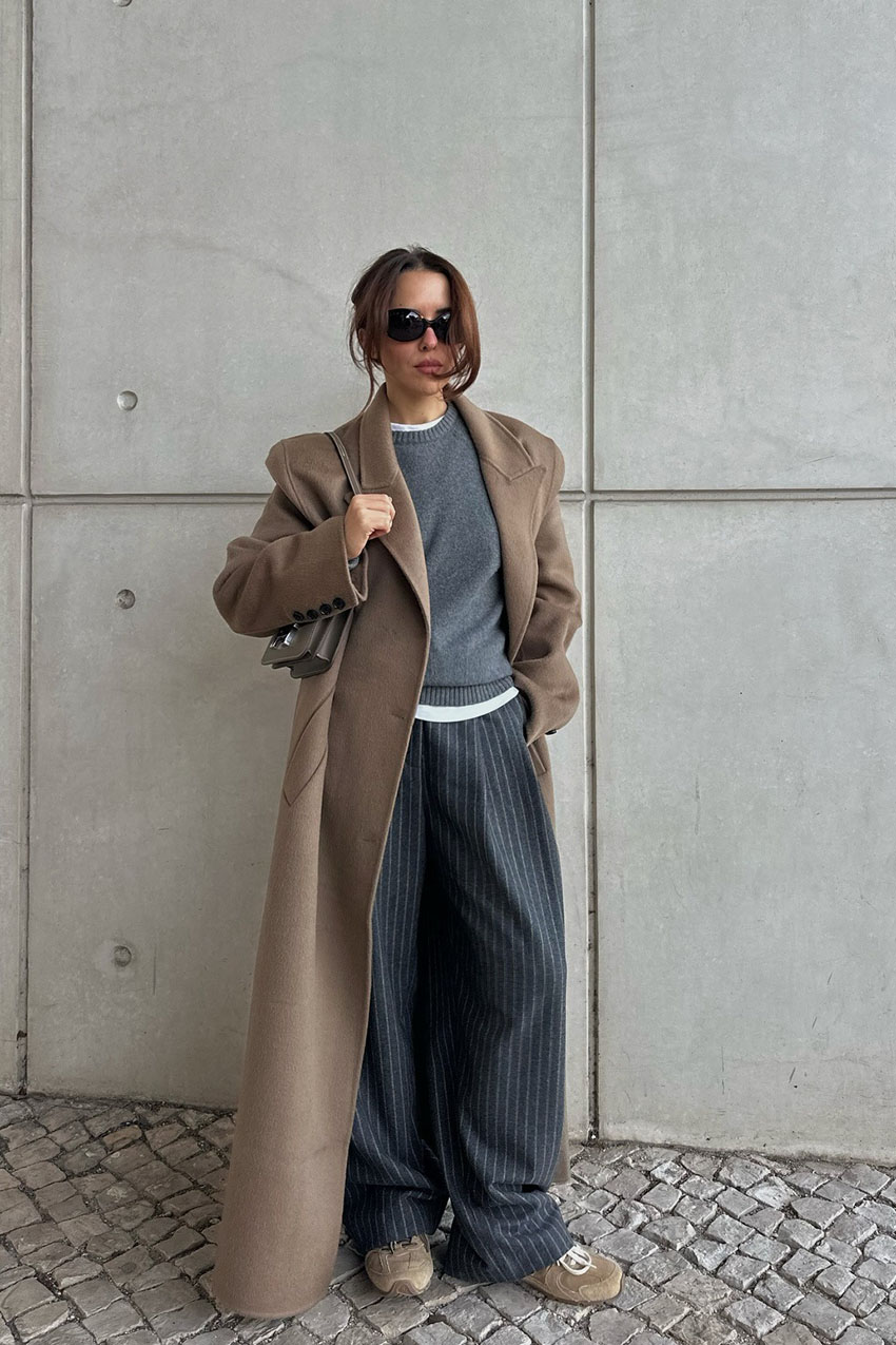 A woman wearing a gray sweater and pants and a beige coat.