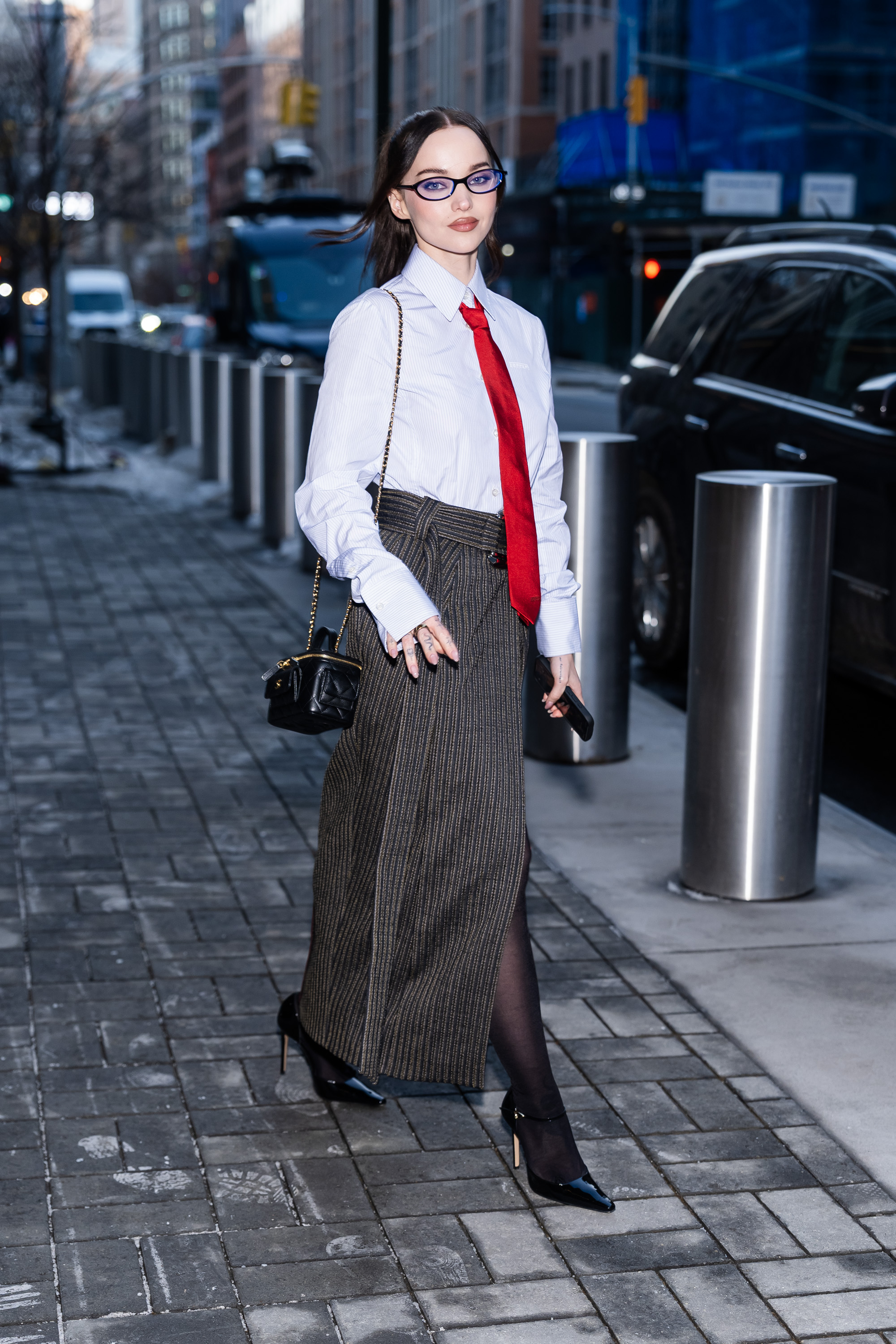 Dove Cameron wearing a button-down, red tie, gray skirt, and black heels.