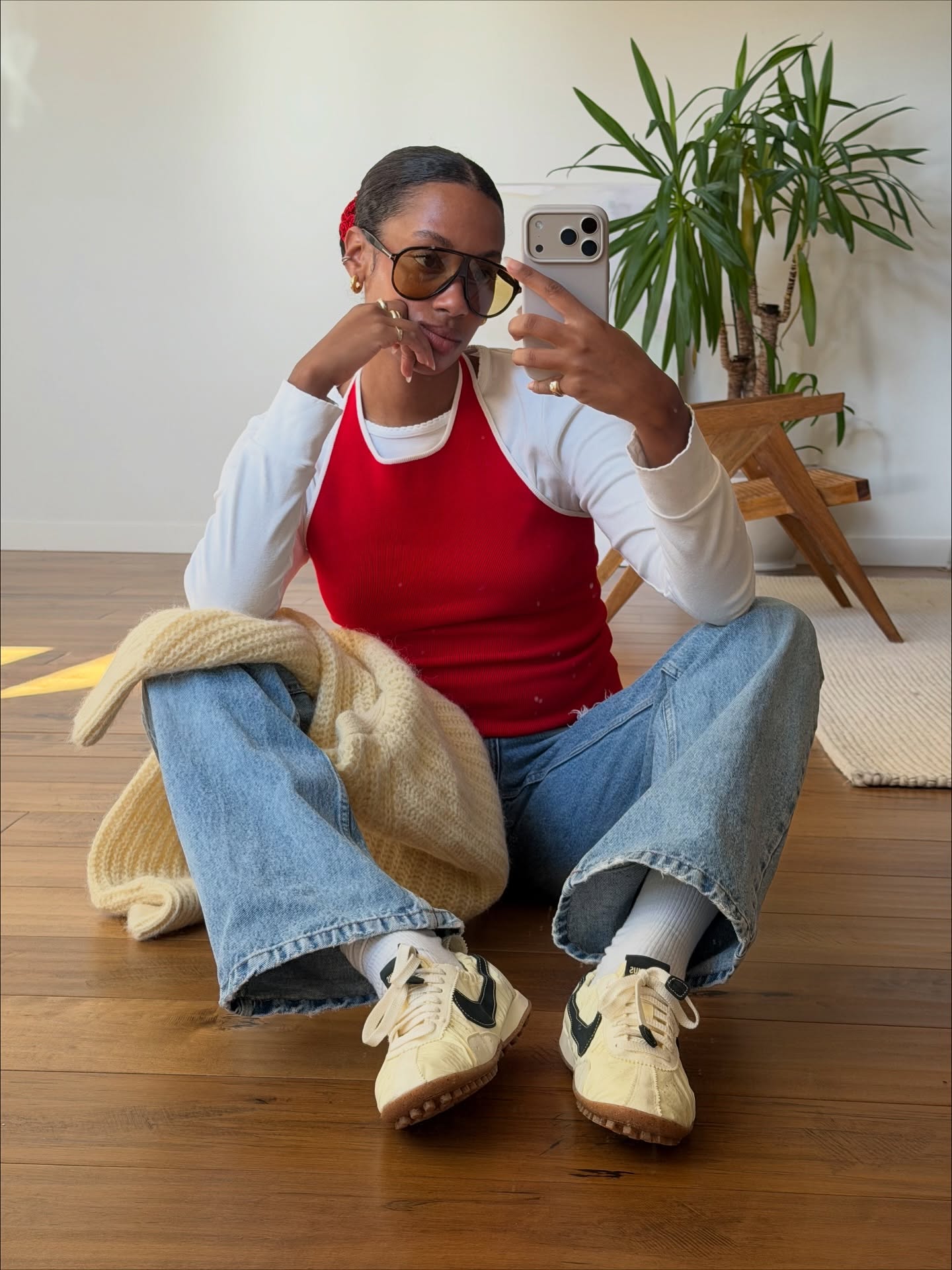 claire most wears a red tank top, white longsleeve, jeans and trainers in a mirror selfie