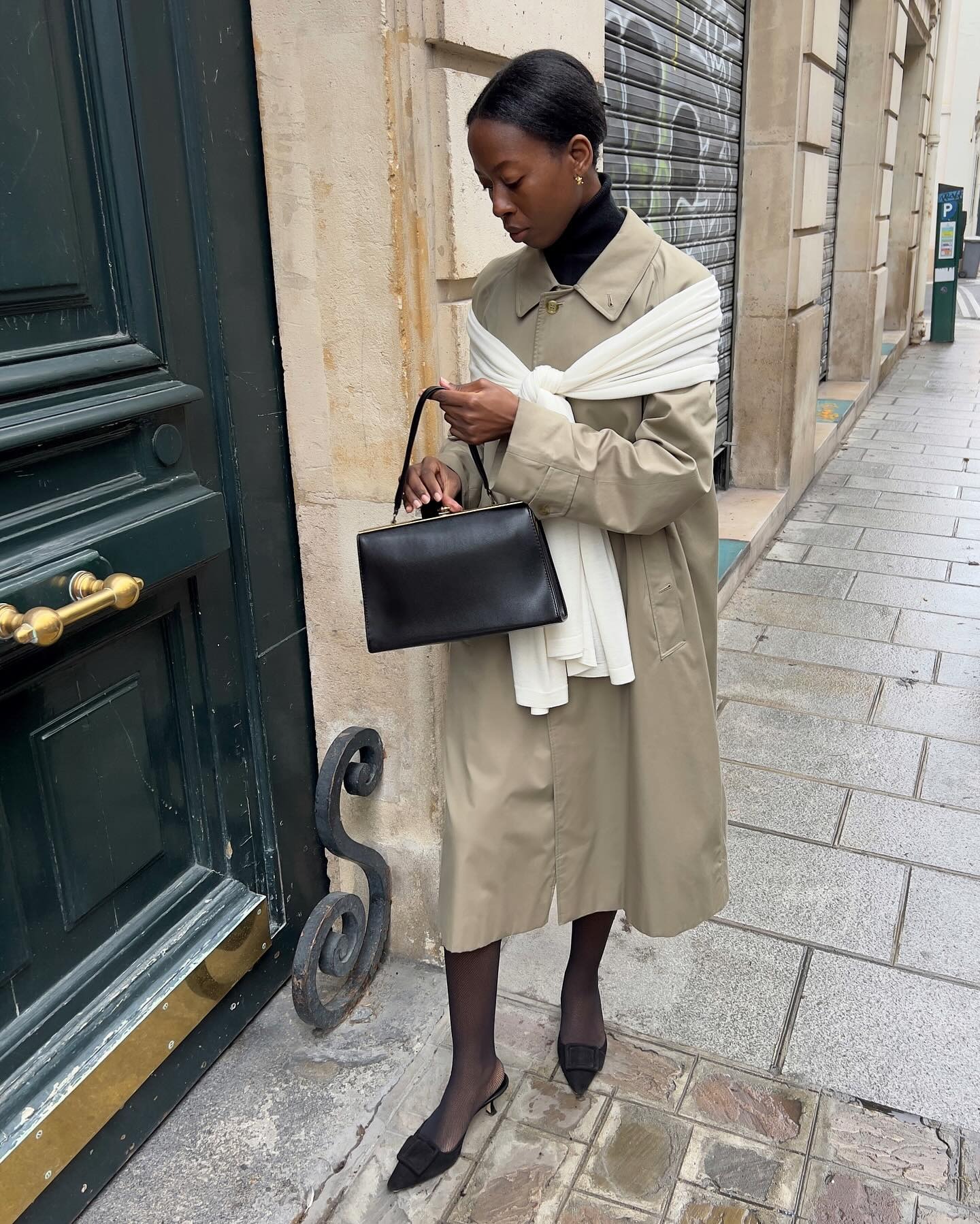@sylviemus_ wearing a trench coat, scarf over the shoulders, vintage kisslock bag, black turtleneck, and kitten heels