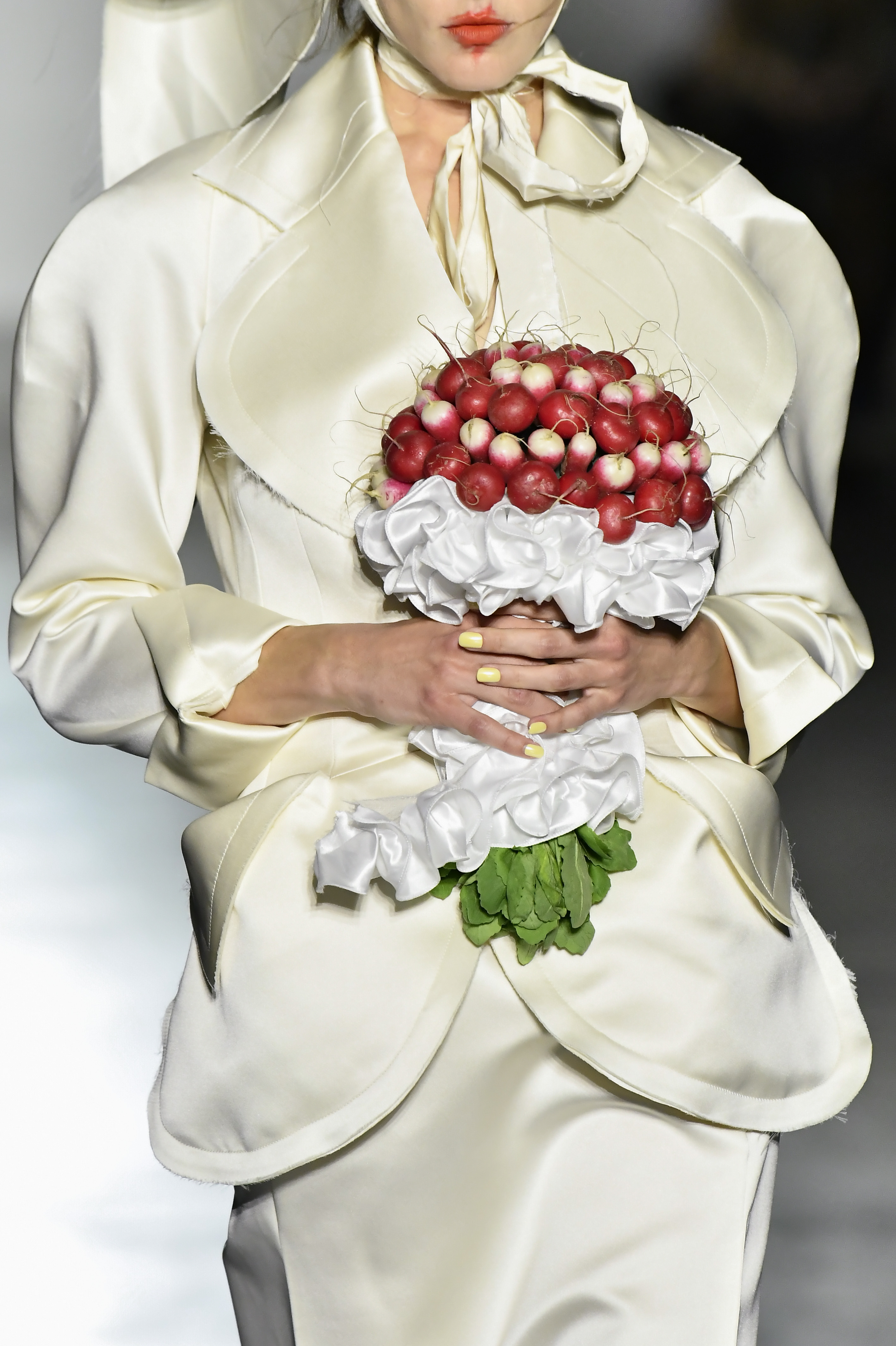 a model wears an ivory skirt suit and carries a radish bouquet.
