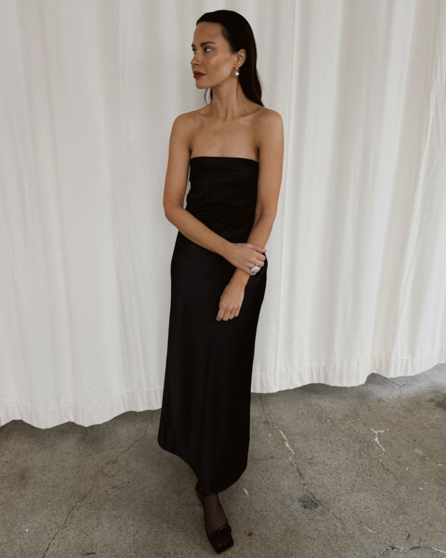style influencer Johanna Piispa poses in a strapless black dress with black tights, and black sandals
