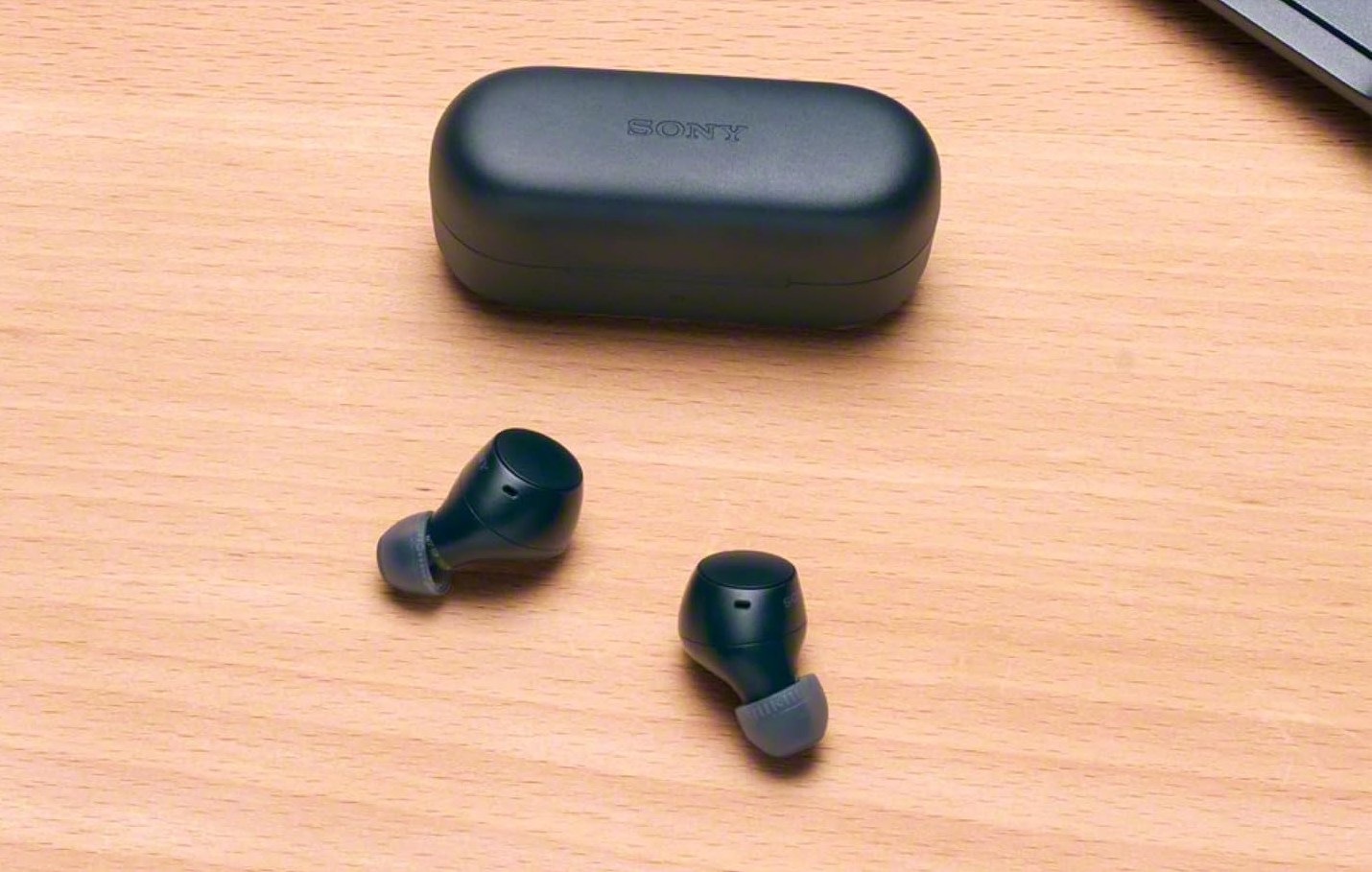 A picture of the Sony WF-C510 earbuds sitting next to their case on a wooden tabletop.