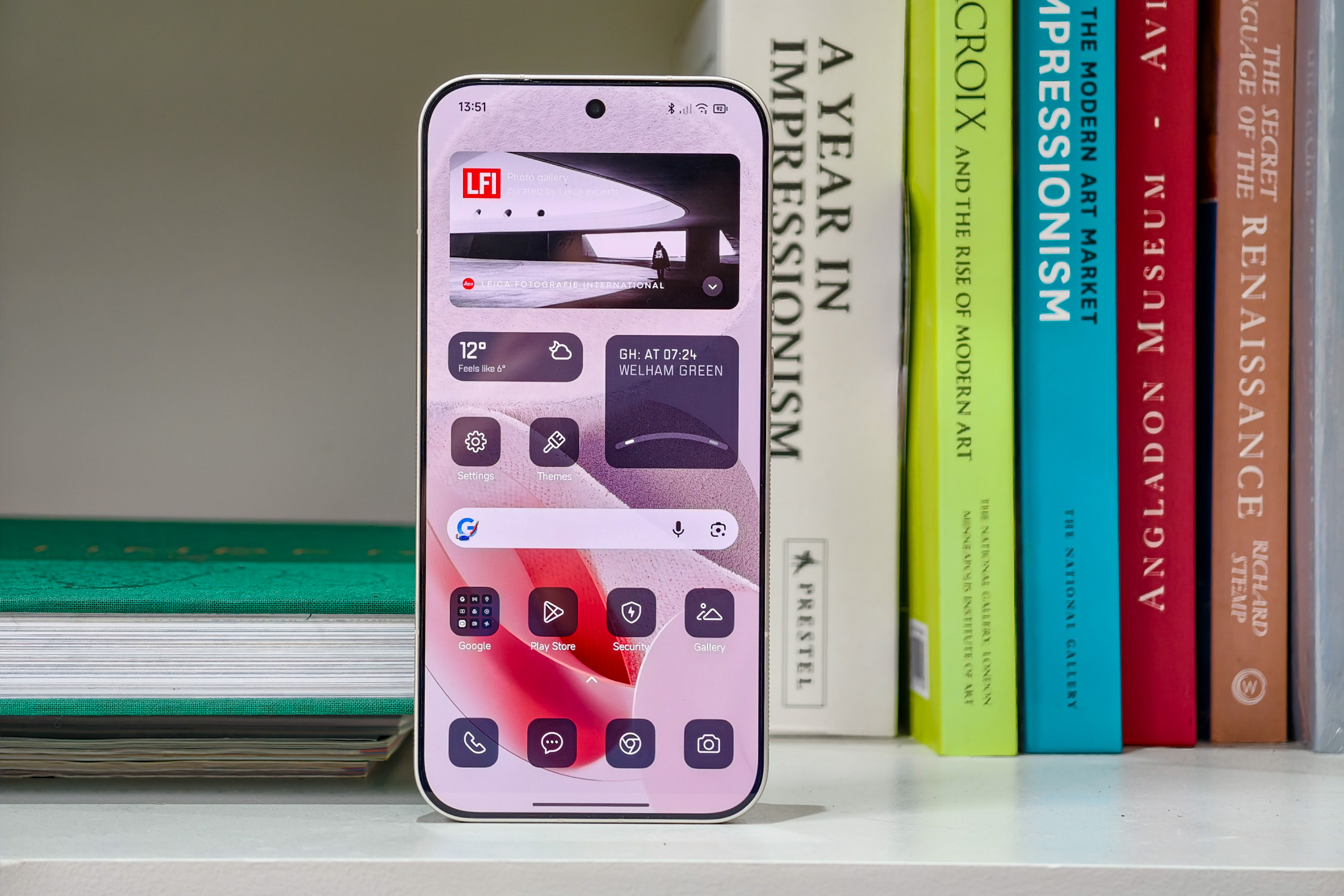 Photo of the Xiaomi Leica Leitzphone on a bookshelf, showing the home screen with monochrome widgets