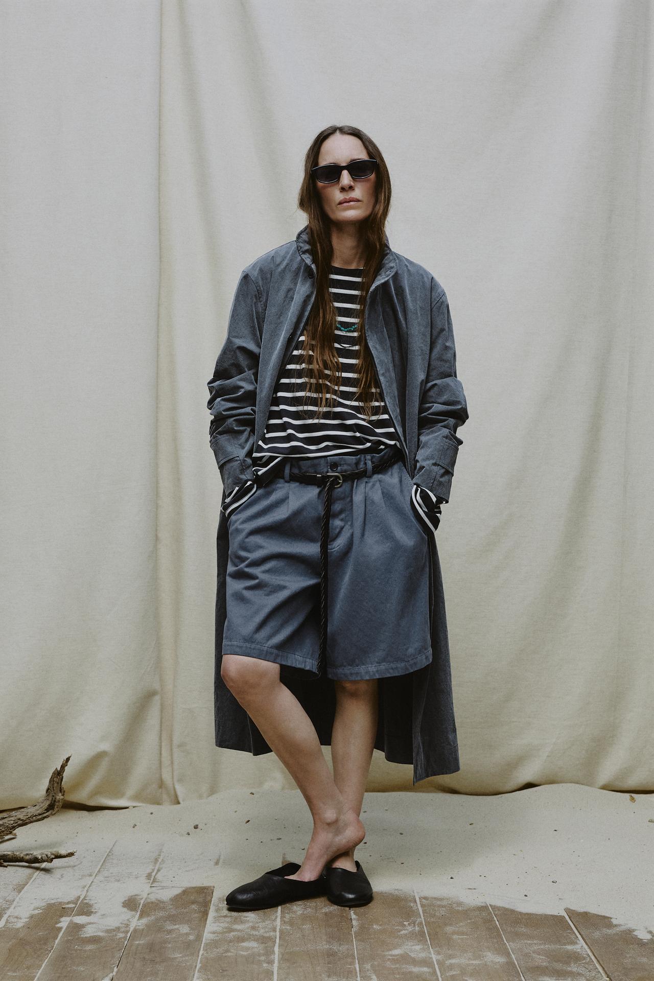 Model wears striped top, trench coat, pleated shorts, and mules.