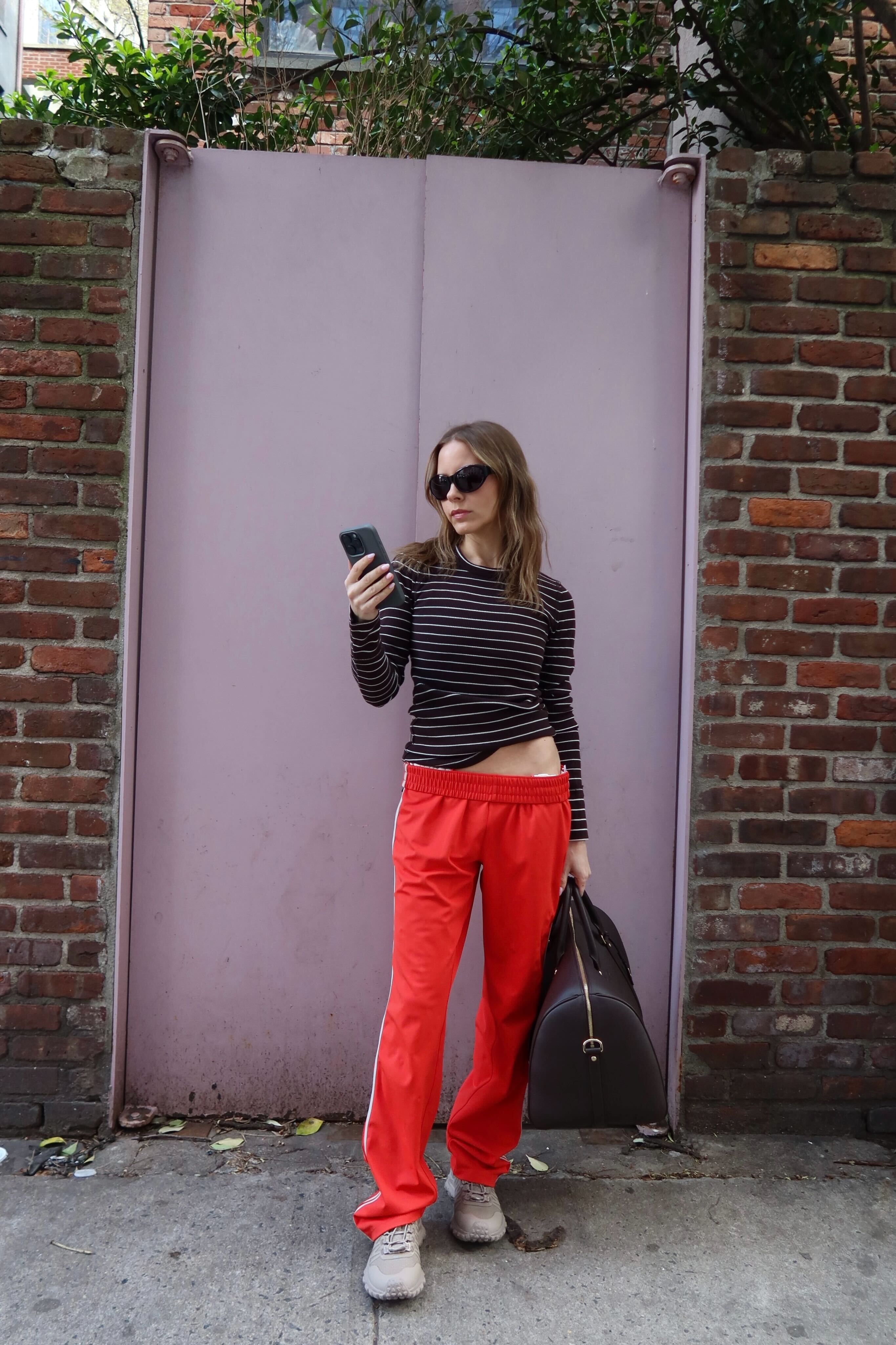 Nikki wears red track pants and alo sneakers.