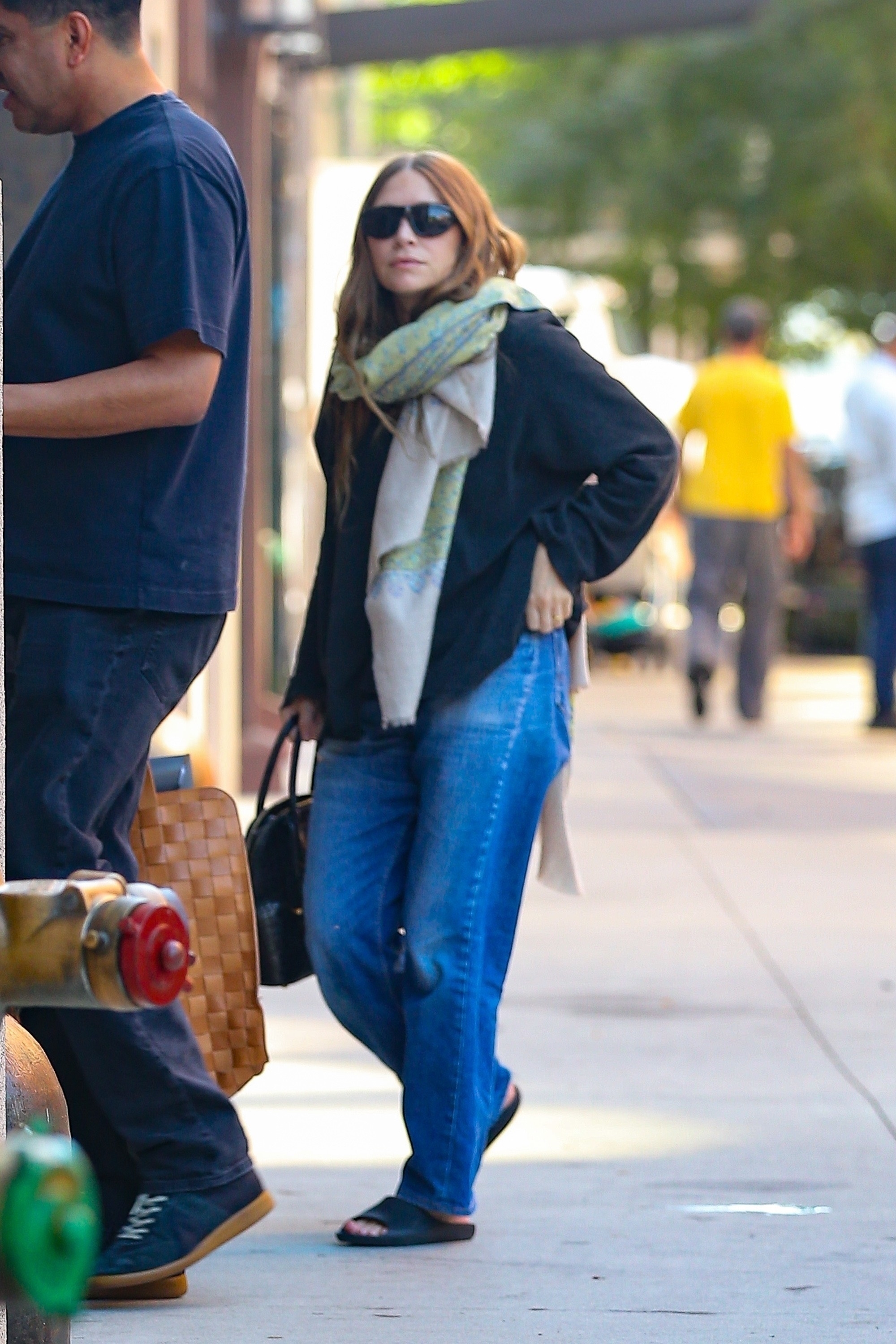 Ashley Olsen wears straight-leg jeans with black slides, a black shirt and an oversized scarf.