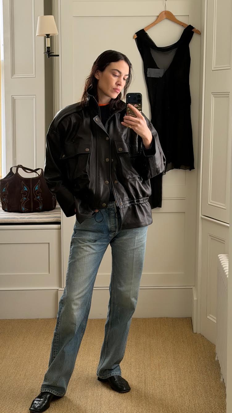 Alexa Chung takes a mirror selfie wearings straight-leg jeans with loafers and a cinch waist leather jacket.