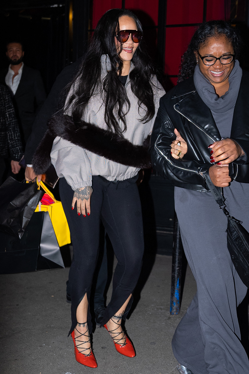 Rihanna wearing black sunglasses, plaid funnel neck jacket, slit leggings, and red lace up pumps.