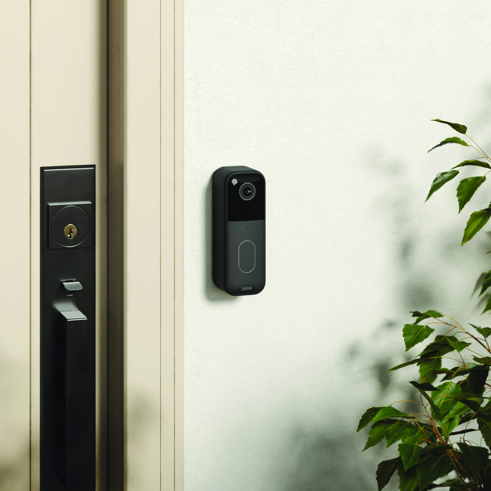 A black video doorbell camera on a white exterior wall next to a front door.