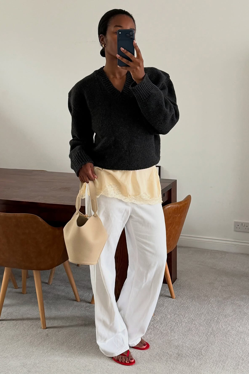 a woman wearing a black sweater, white jeans, and red flip flops