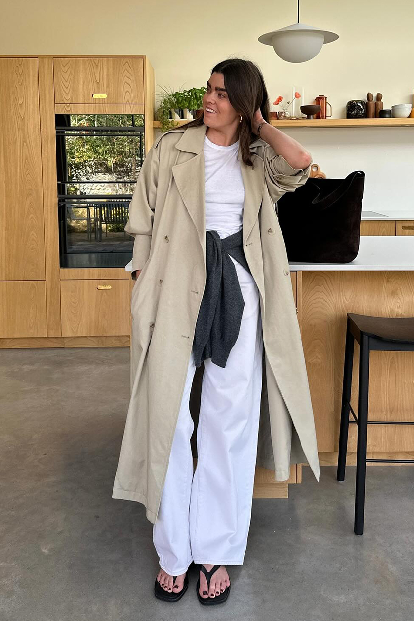 a woman wearing a trench coat, white jeans, and black flip flops