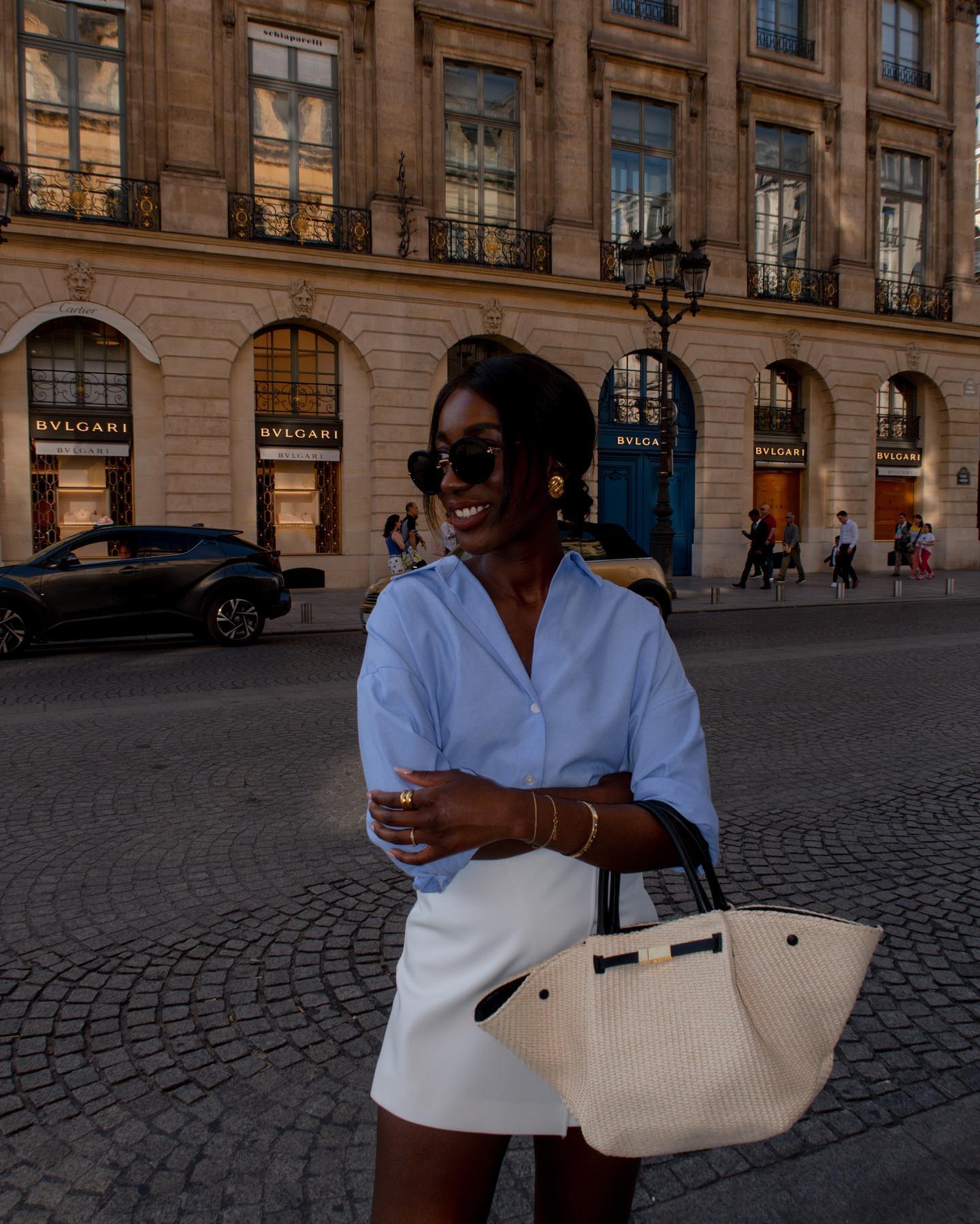 Aida wearing a blue shirt, white skirt and raffia woven bag.