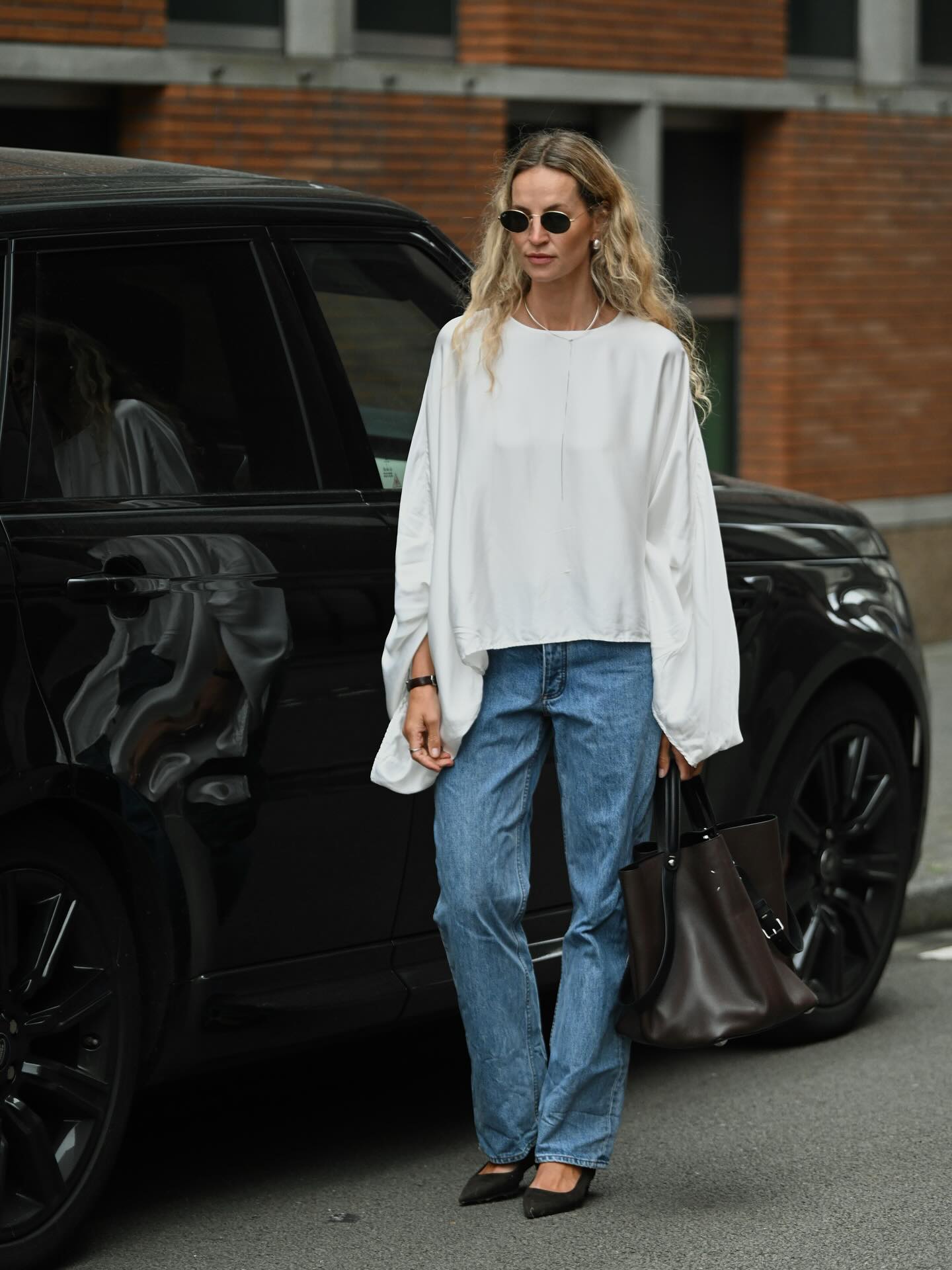 Anouk wearing a white top, blue jeans and round sunglasses.