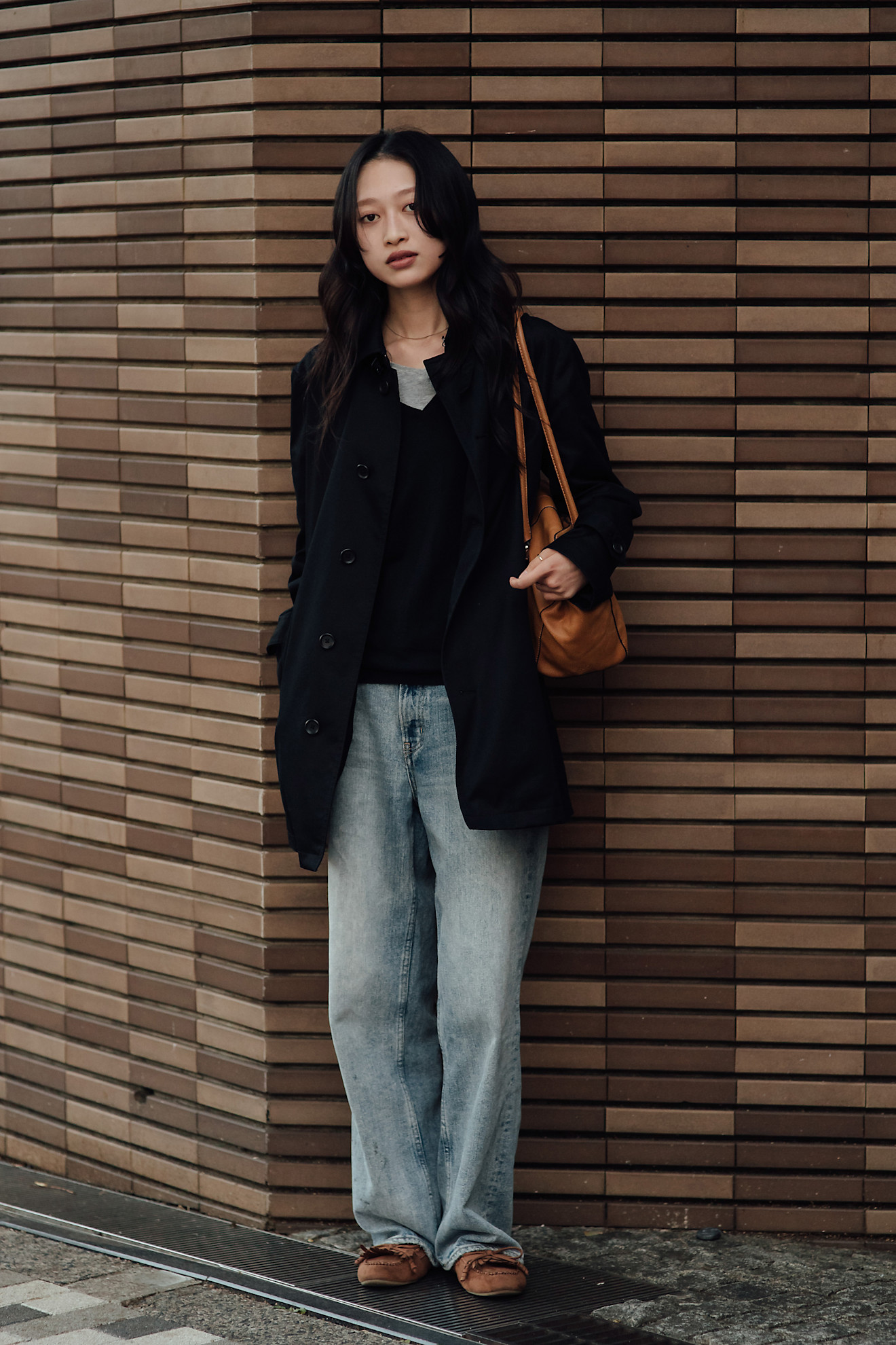 A woman wears a black jacket, jeans, and flats.
