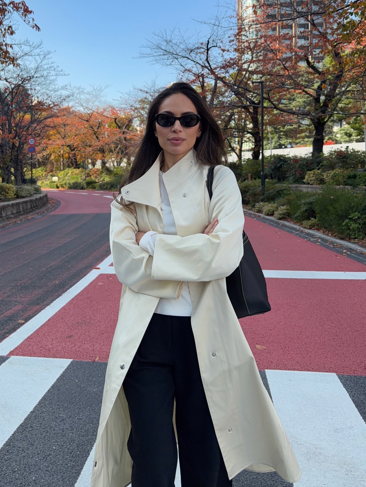 Marianna wears a trench coat, white tee, and black trousers.